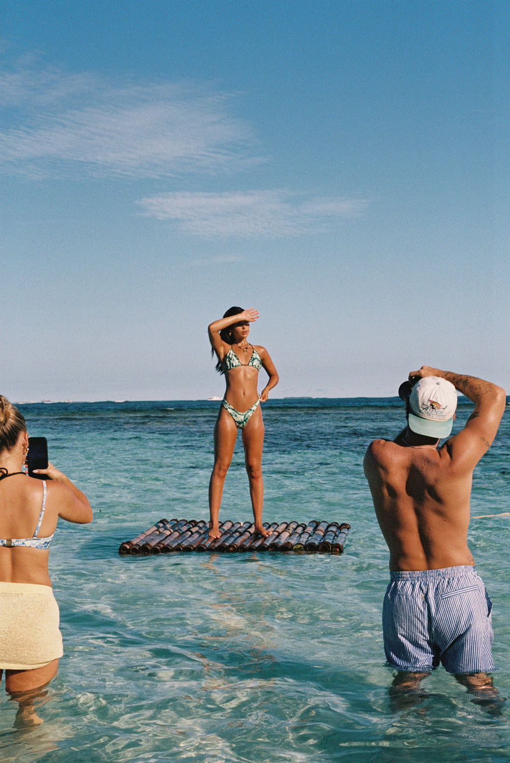 People on a beach with one person standing on a raft and others taking photos.