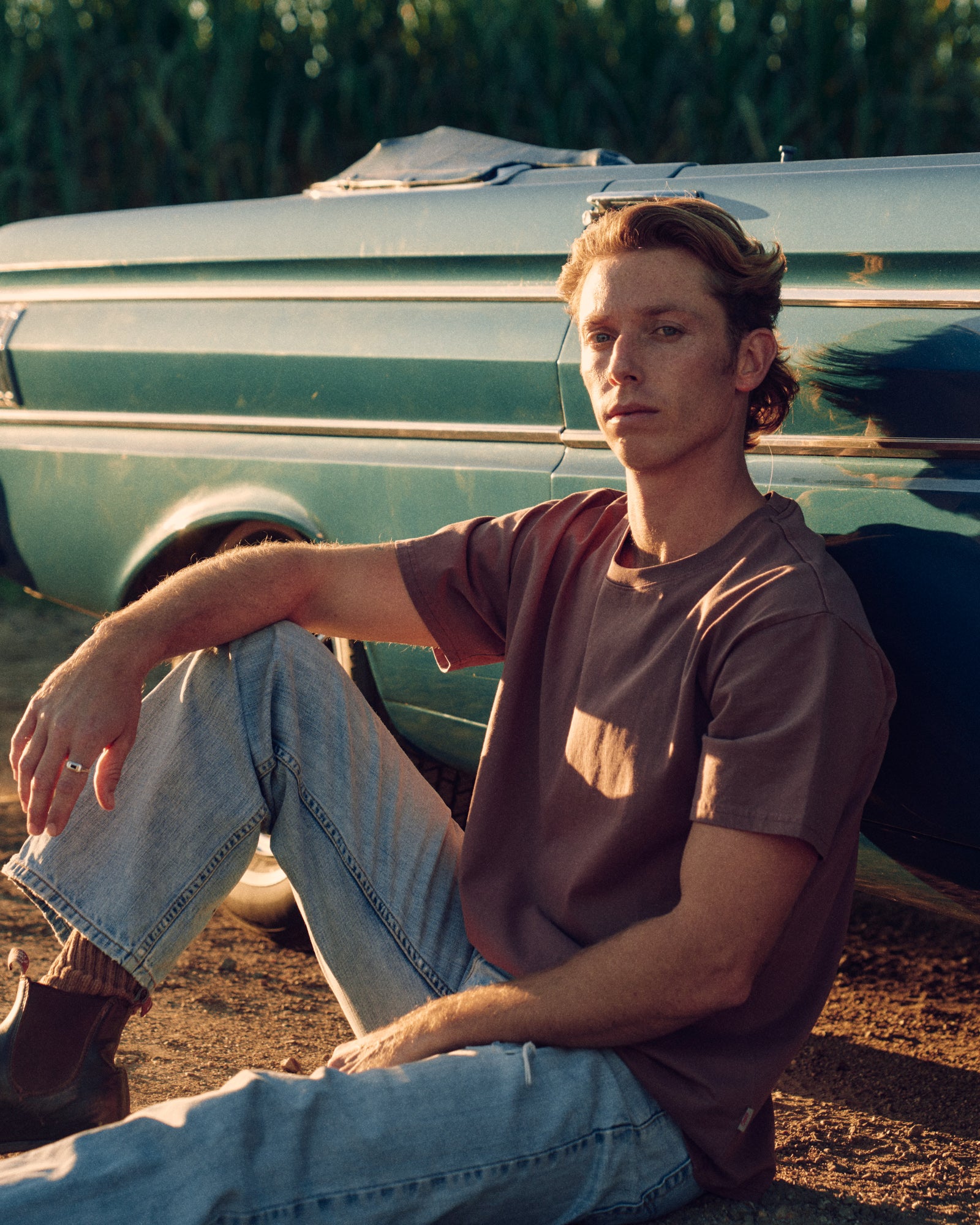 Man sitting on the ground next to a green truck with cornfield in the background