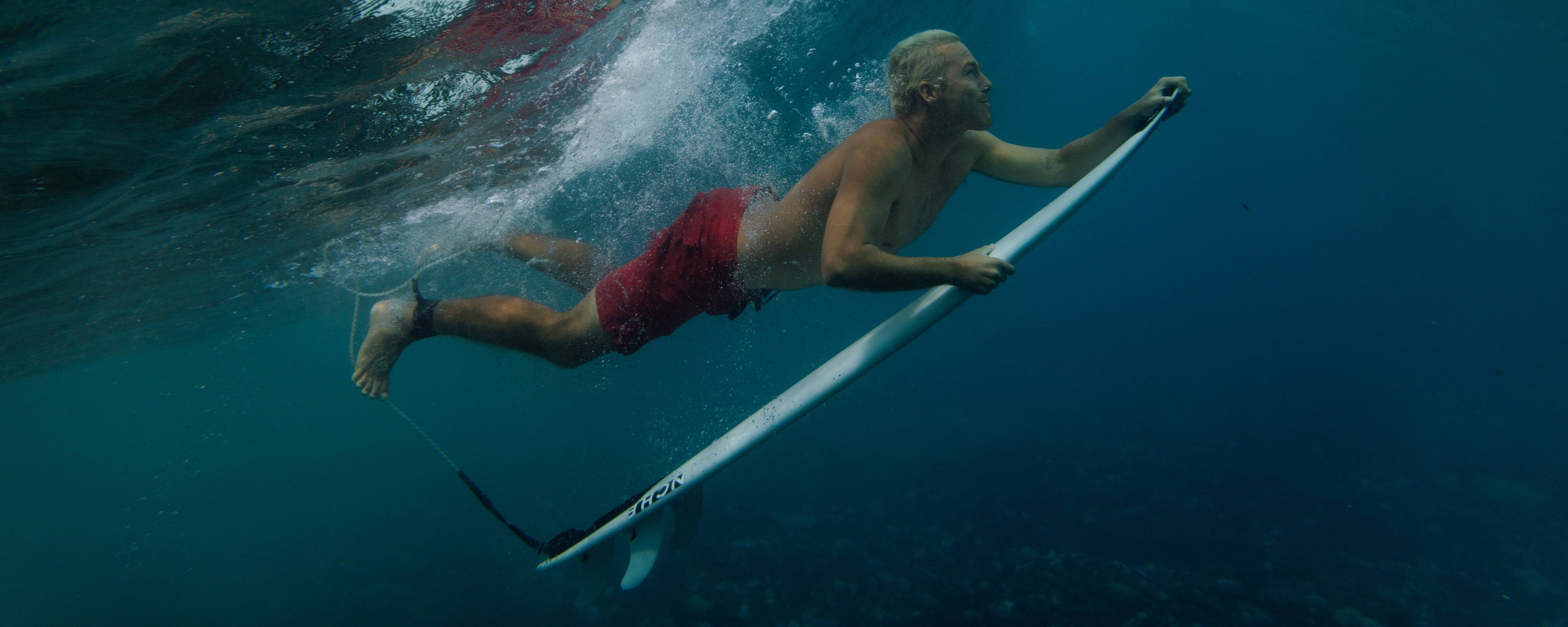 man diving under a wave with a surfboard