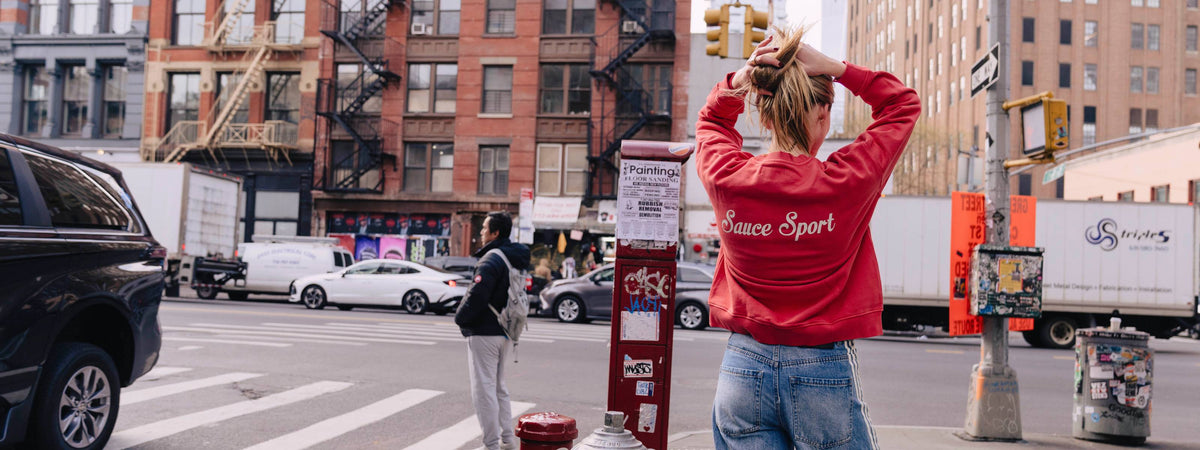 Woman standing in New York City with a red sweatshirt saying SAUCE SPORT