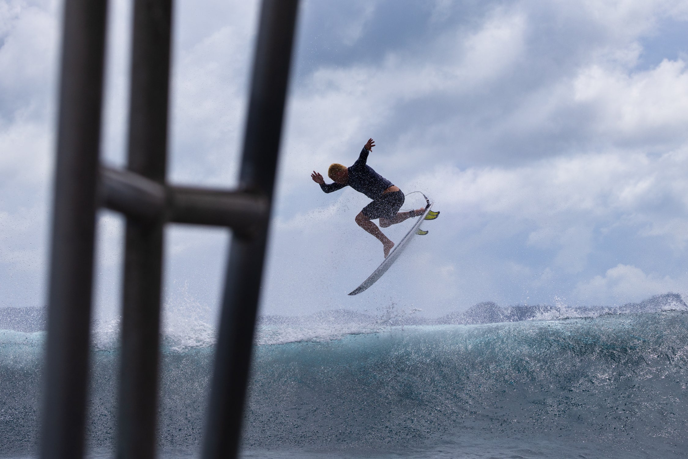 Surfer performing a trick on a wave with a cloudy sky in the background
