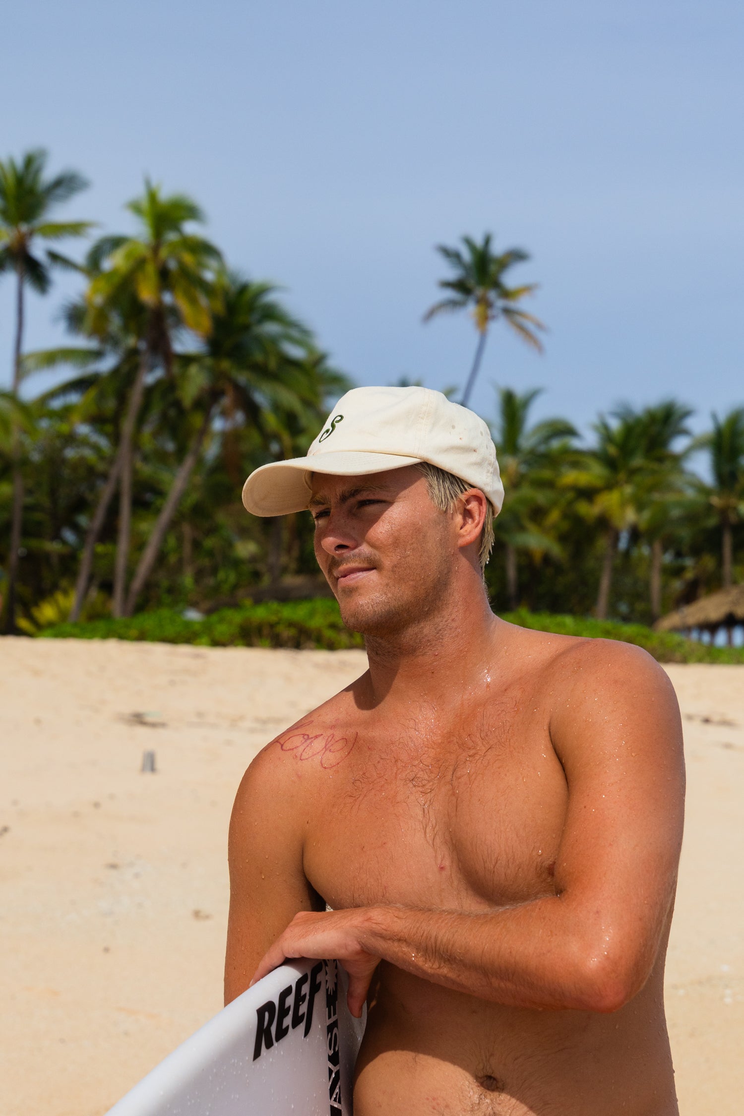 Man on a beach holding a surfboard with palm trees in the background