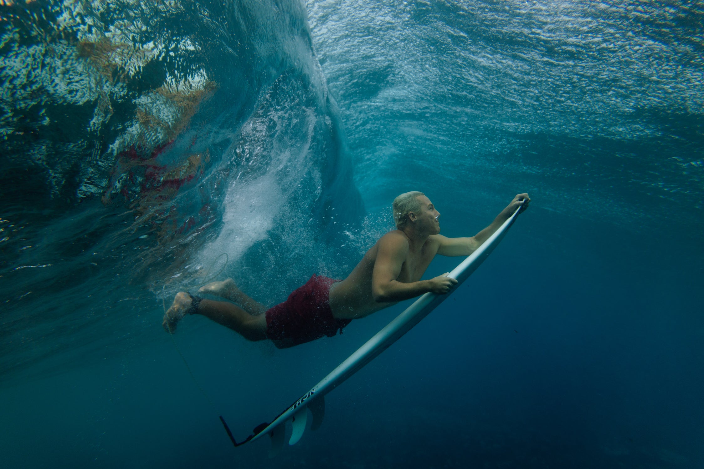 Person swimming with a surfboard underwater in clear blue water