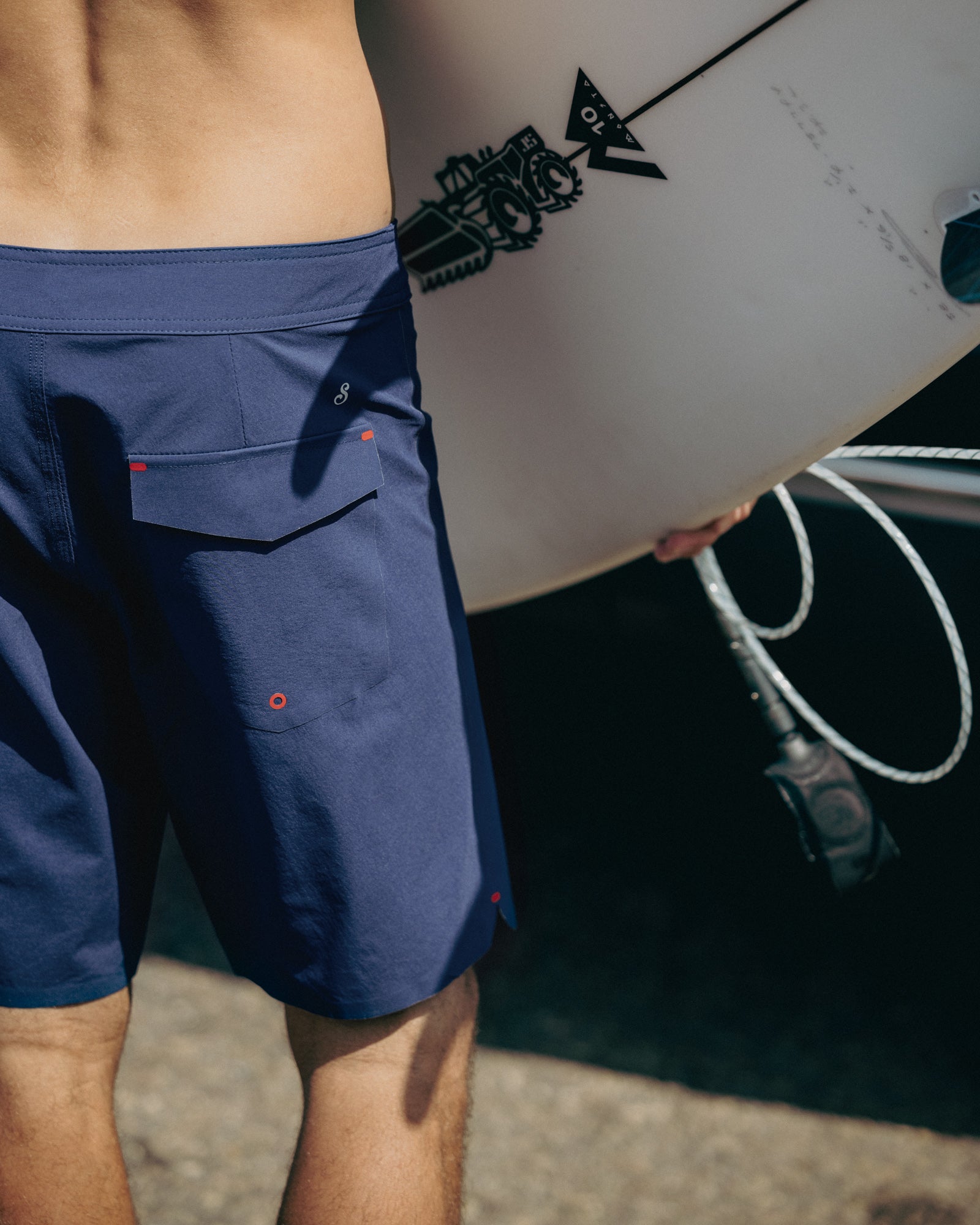 Person wearing blue shorts holding a white surfboard with black graphics.