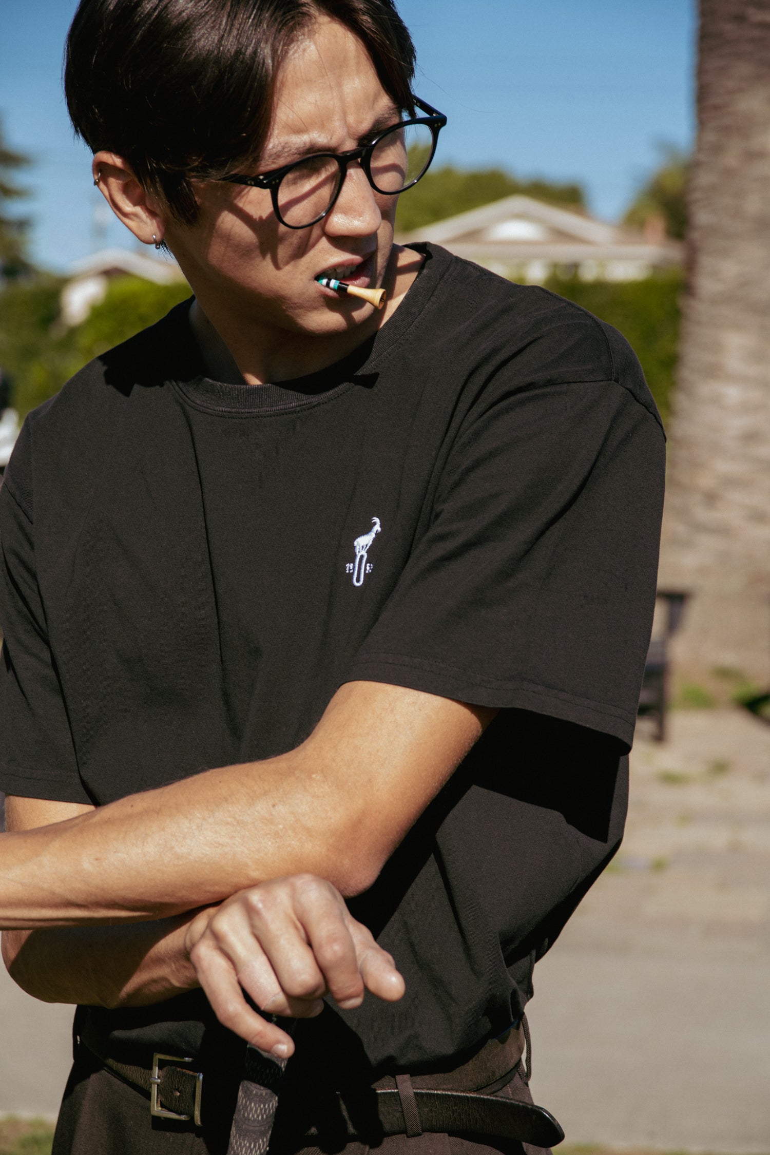 Person wearing a black t-shirt with a logo, standing outdoors with palm trees in the background.