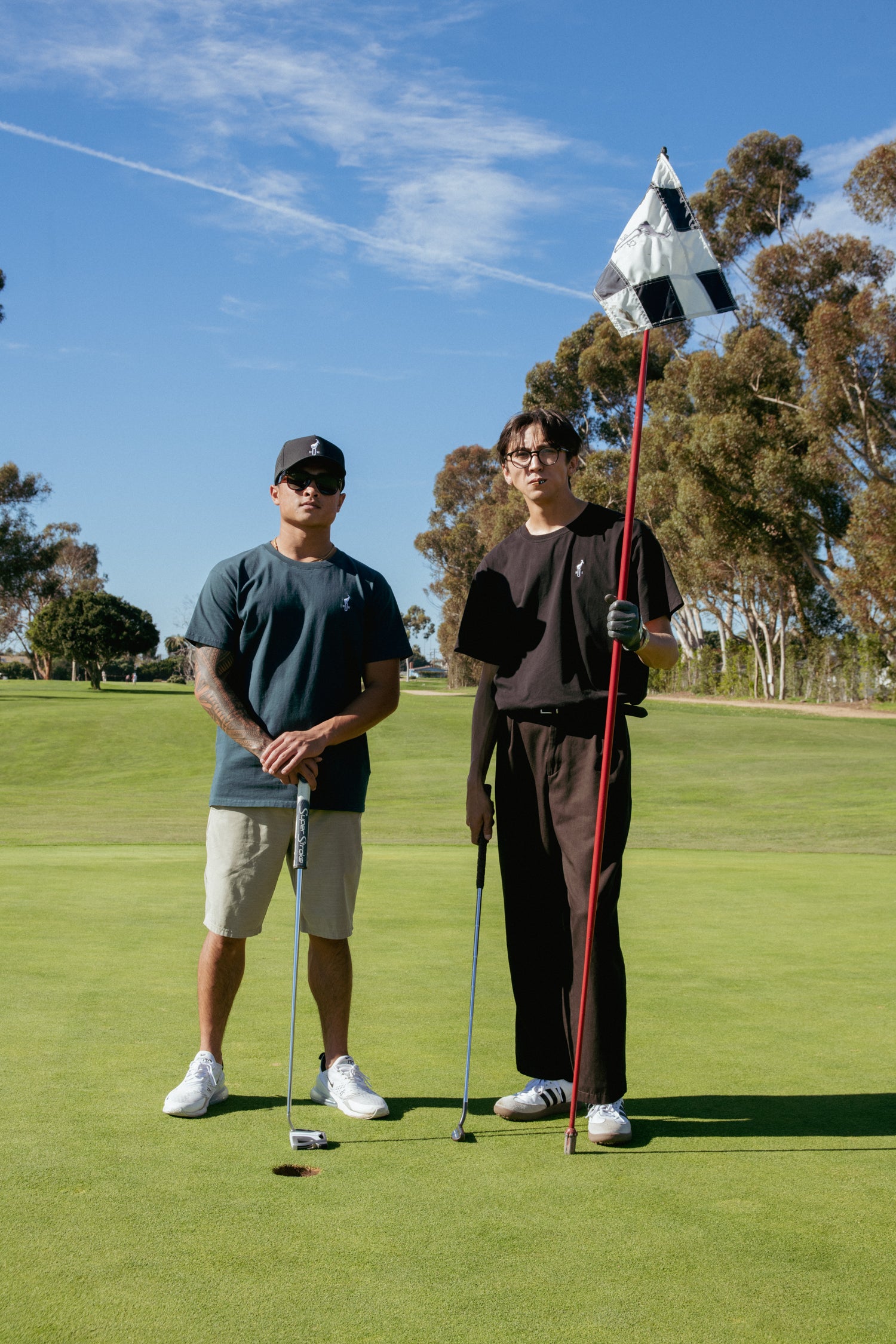 Two men on a golf course with one holding a flag and a golf club.