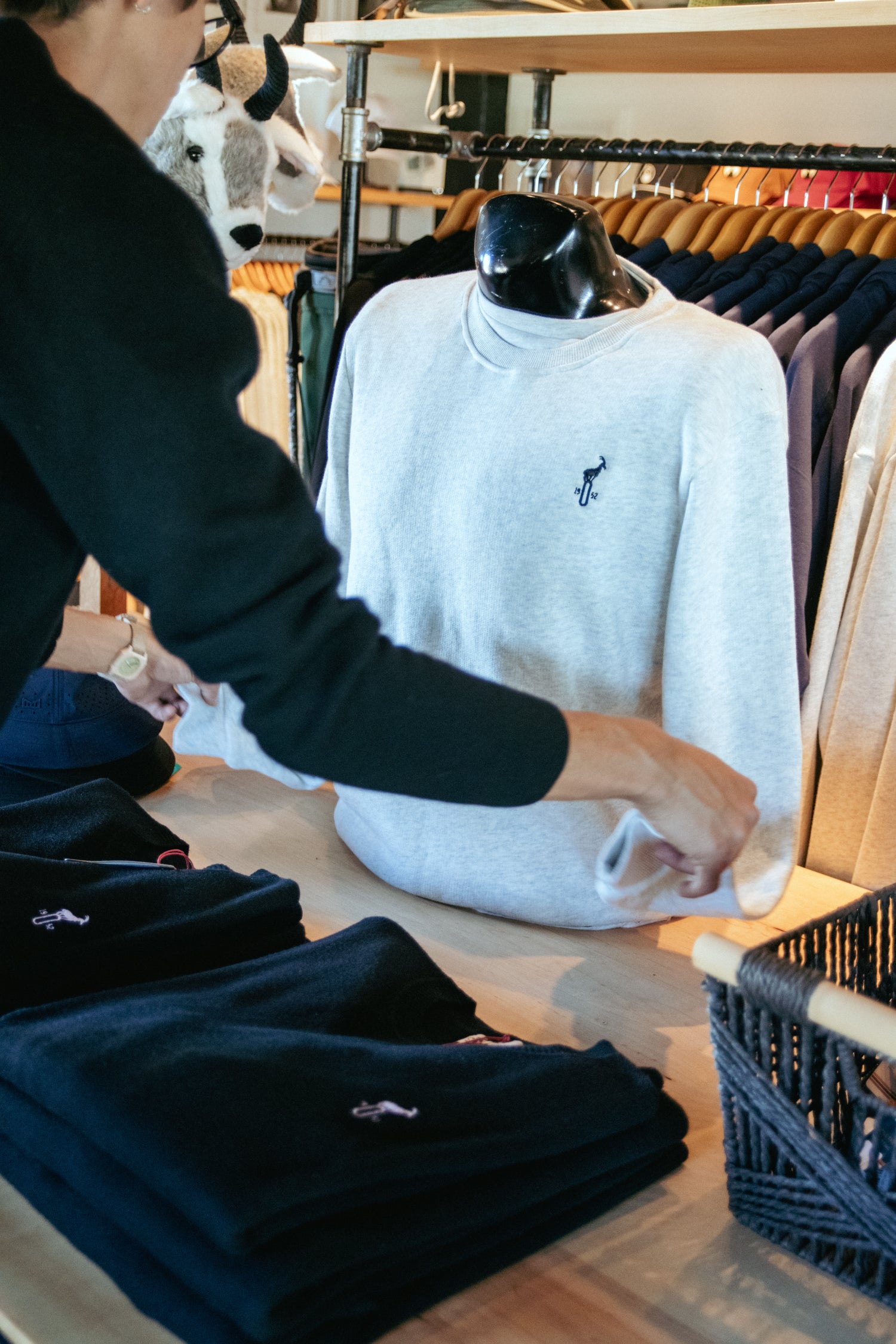 Person interacting with folded clothes and a white sweatshirt on a table in a store setting.