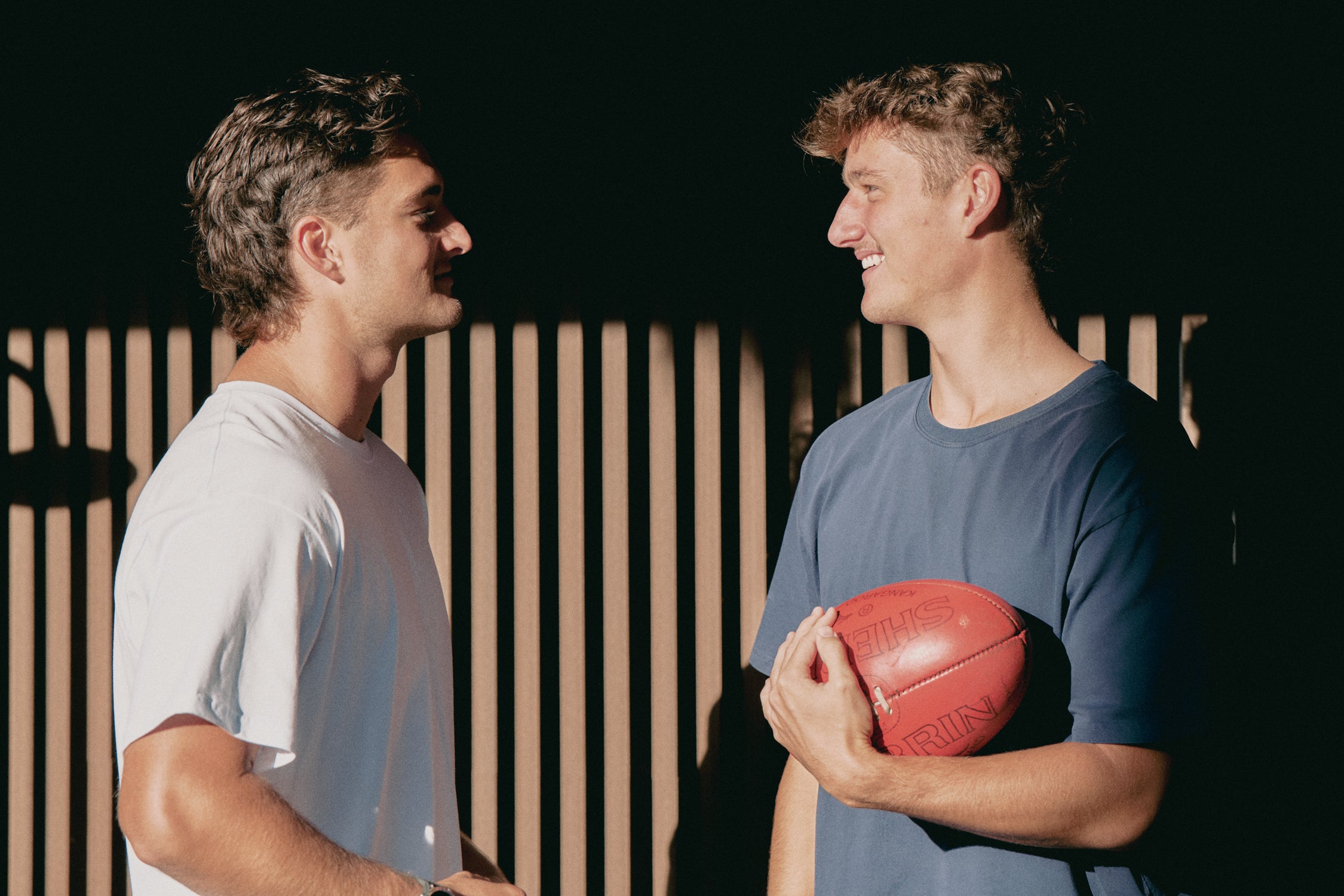 Two men standing next to each other, one holding a football.