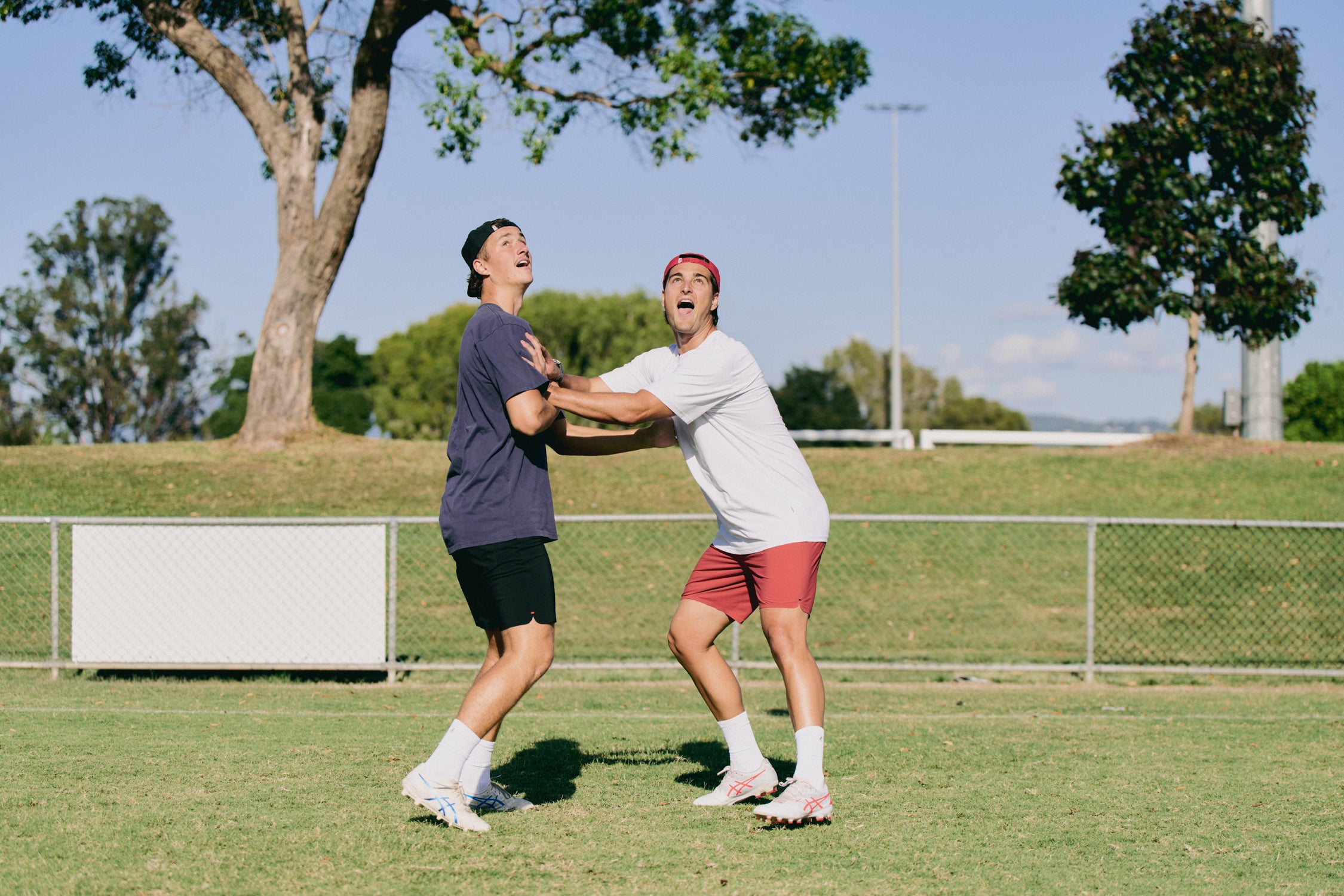 Two people playing a game of catch on a grassy field with trees and a clear sky in the background.