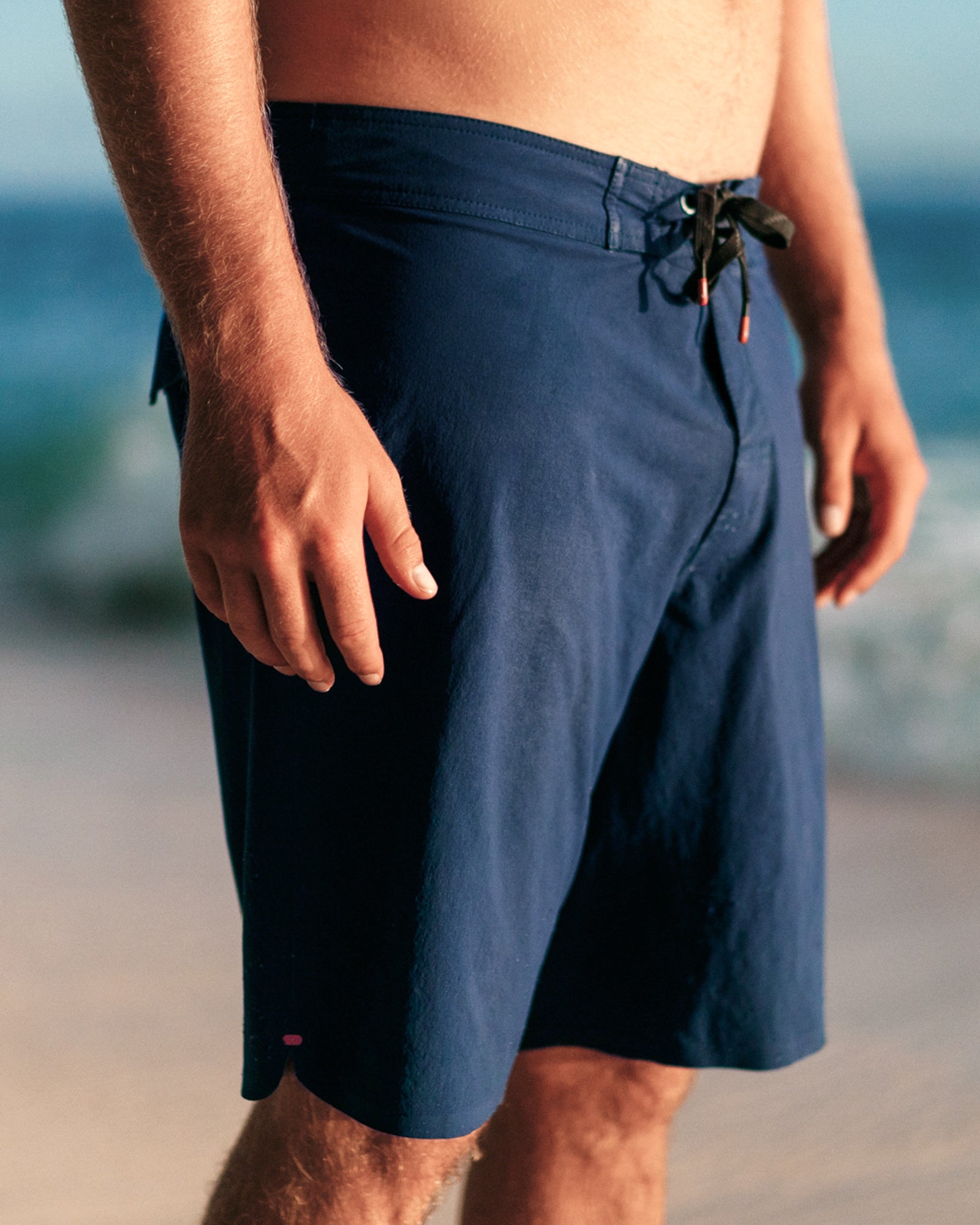 Person wearing navy blue shorts on a beach with blurred ocean background