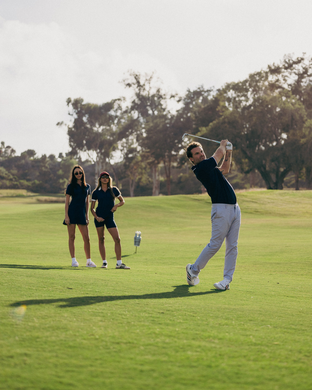 Man playing golf on a green course with two women watching.