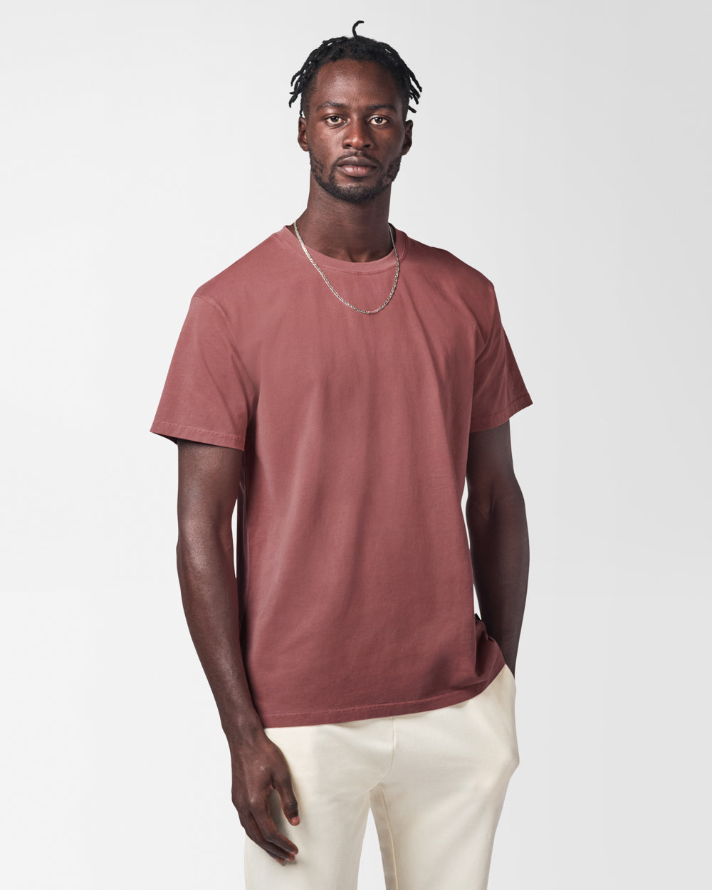 Man wearing a maroon t-shirt, white jeans and silver chain on a white studio background