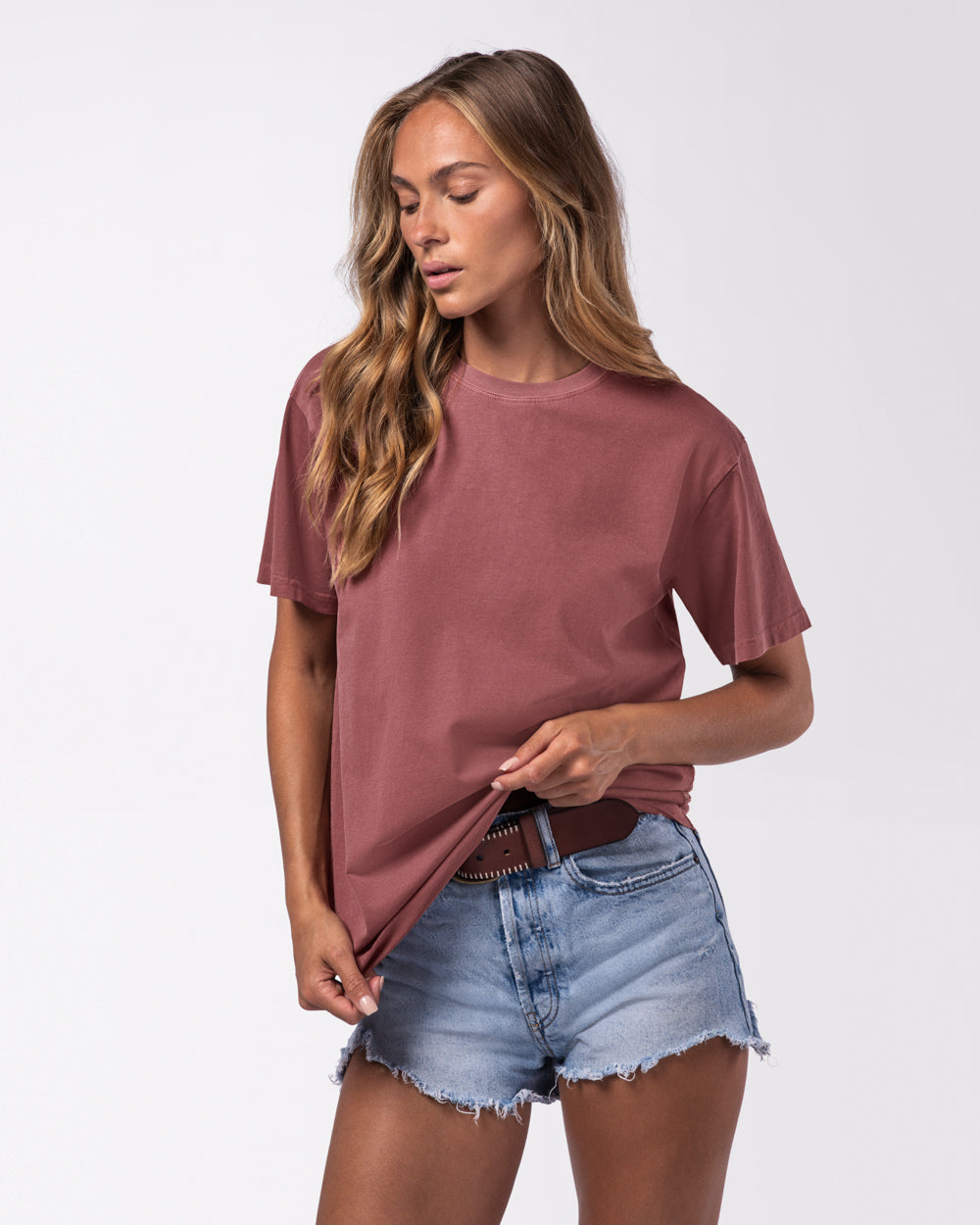 Female model wearing denim shorts and a maroon oversized t-shirt on a white studio background