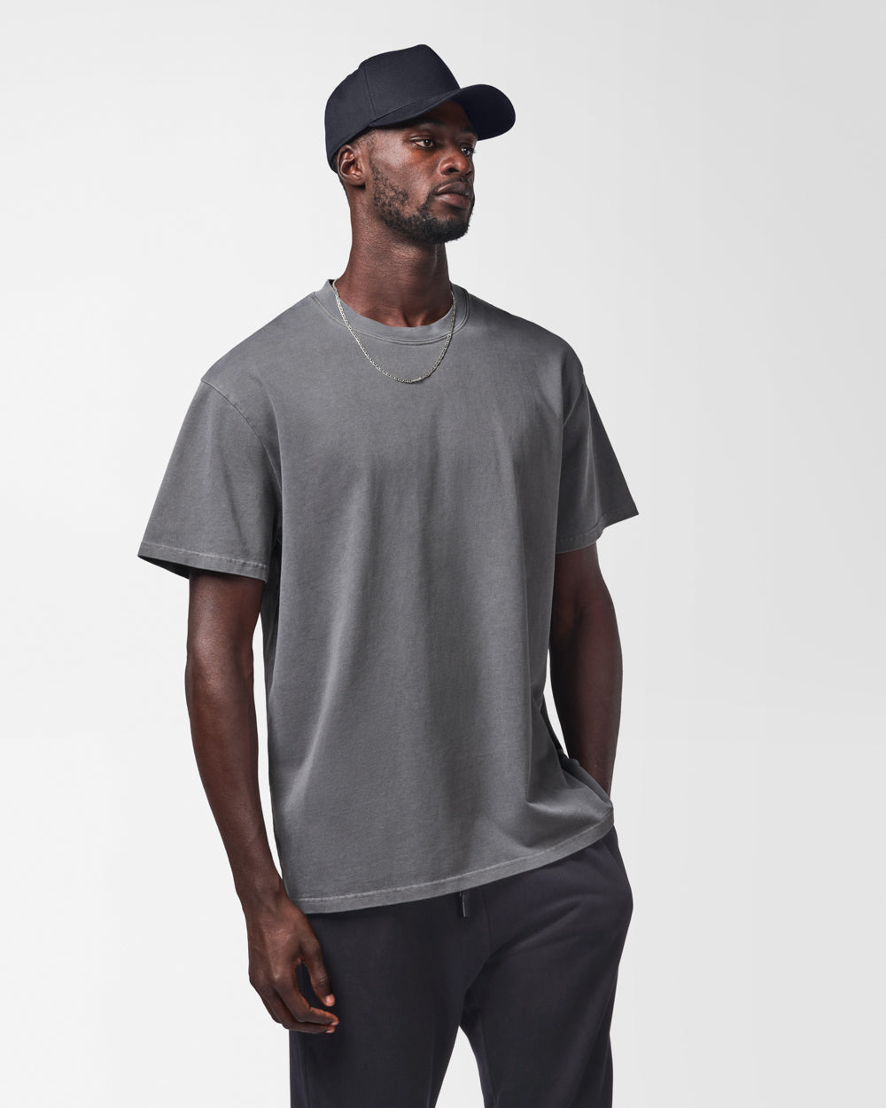 Man wearing a dark grey t-shirt with a black cap on a white background