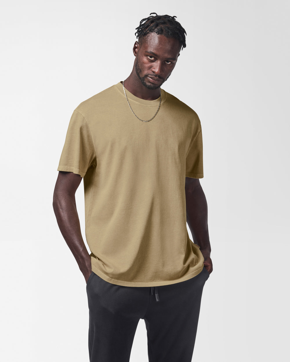 Man wearing beige t-shirt with black sweat pants on a white background.