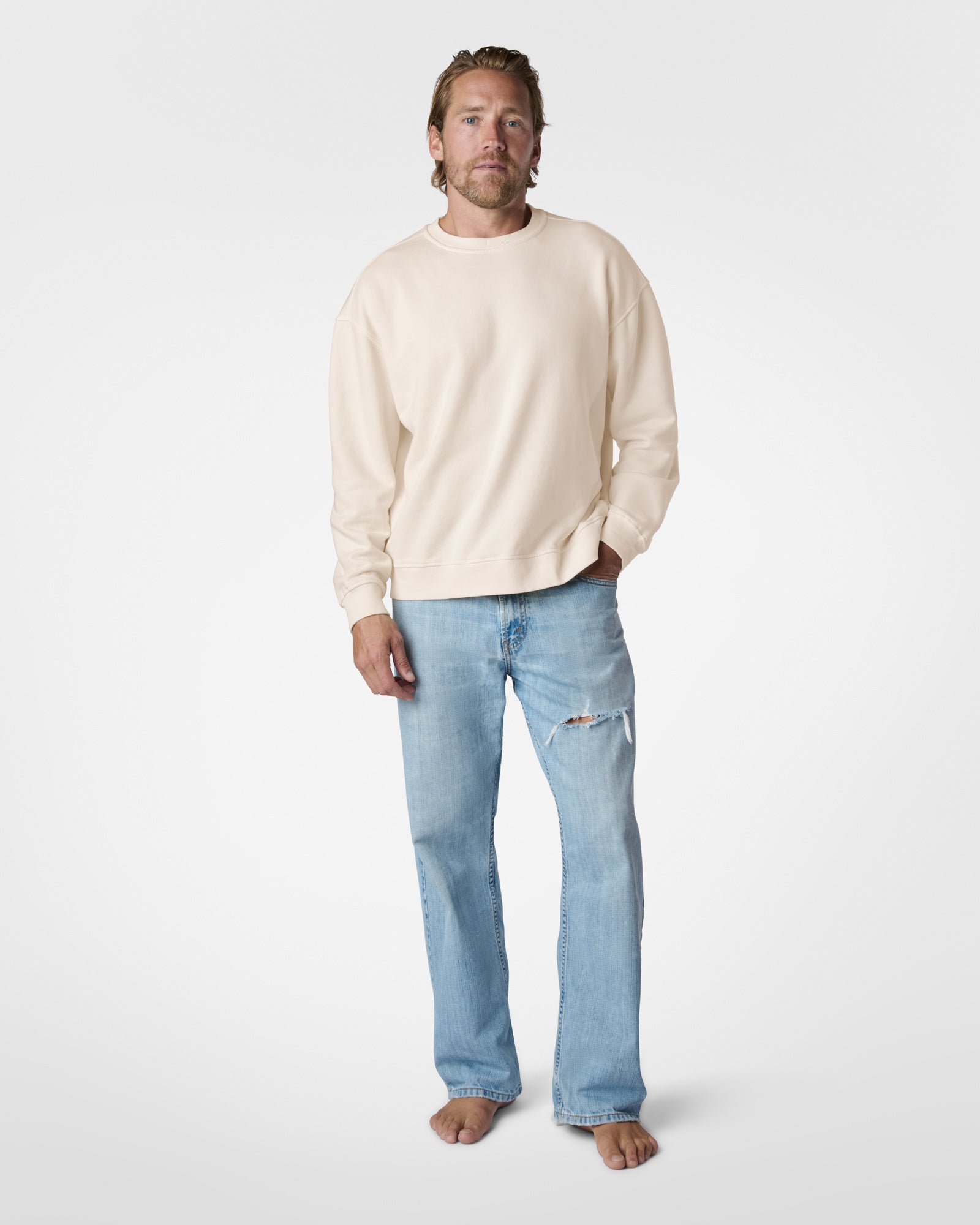 Man wearing a beige sweater and light blue jeans on a white background