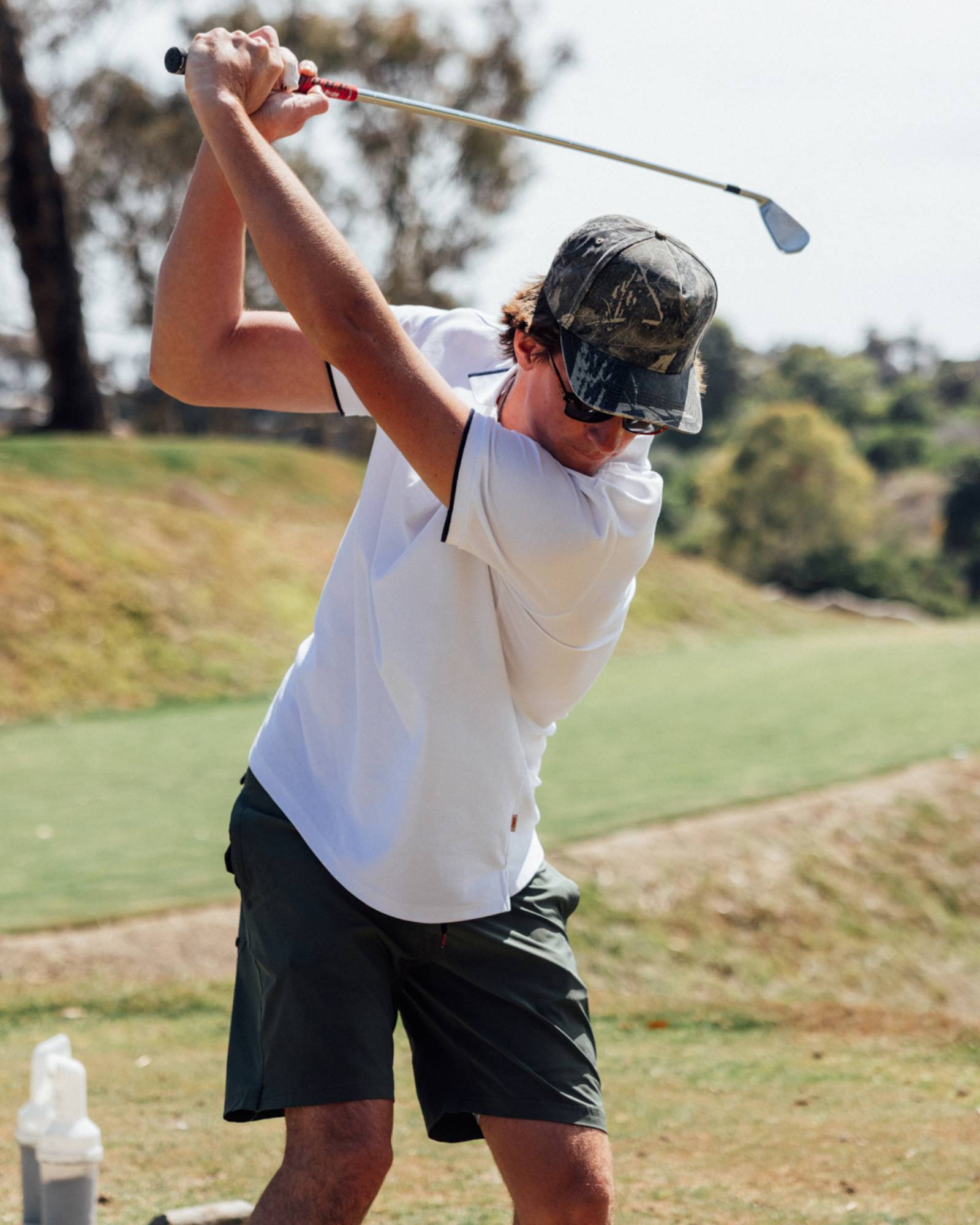Man swinging a golf club and wearing a white polo