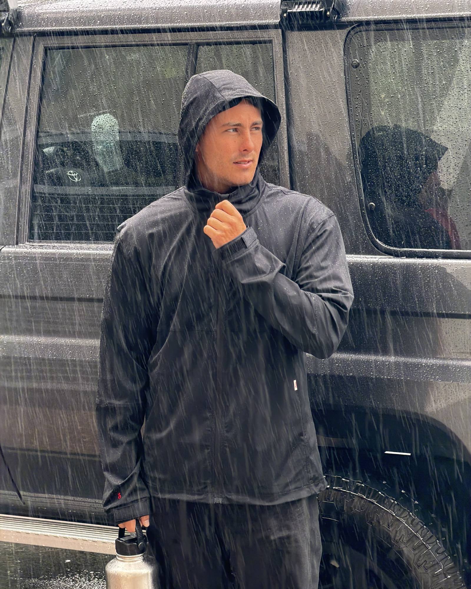 Person wearing a raincoat standing next to a vehicle in the rain