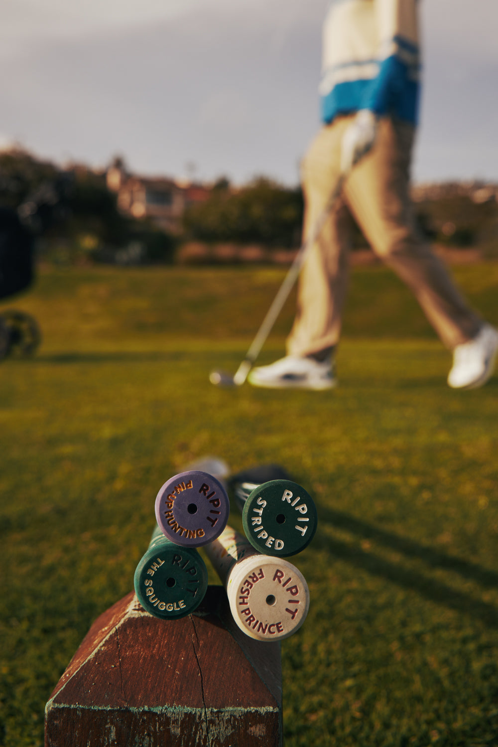 Close-up of golf club heads with a blurred golfer in the background on a golf course.