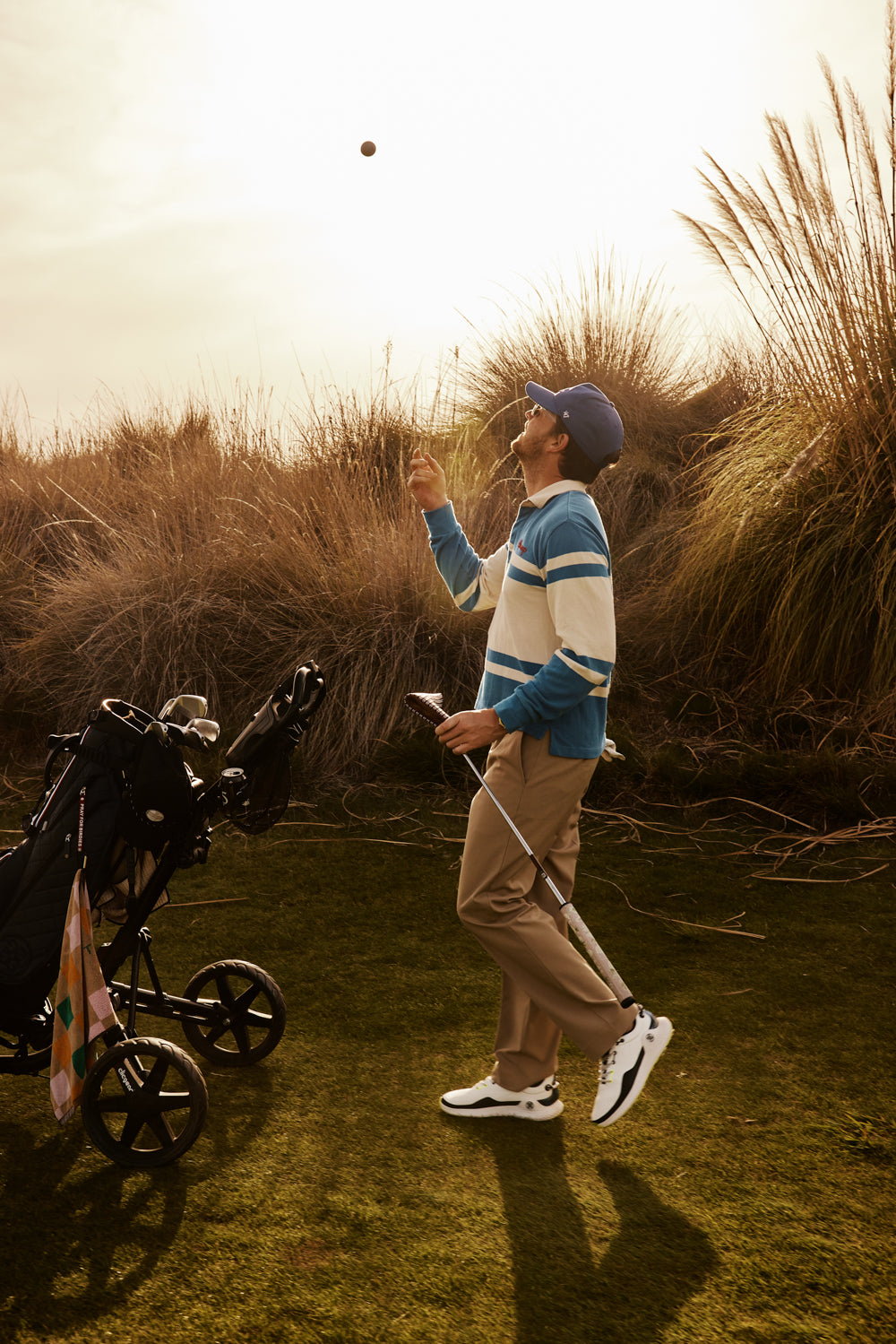 Person standing in a grassy field with a stroller nearby, holding a phone.