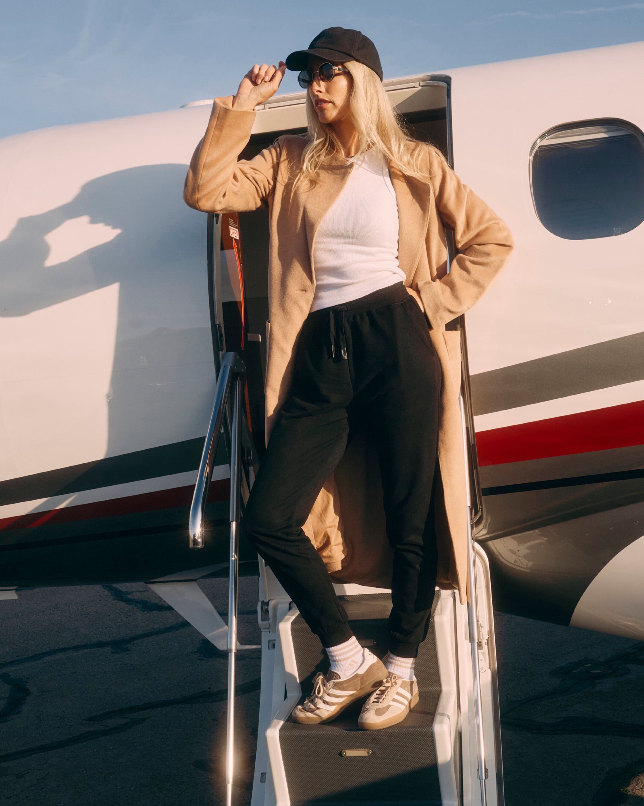 Person in a beige coat and black cap stepping off a private jet.