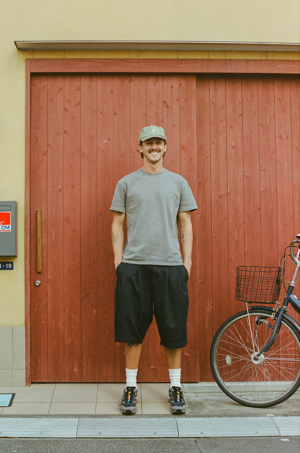 Man standing next to a bicycle in front of a red wooden door