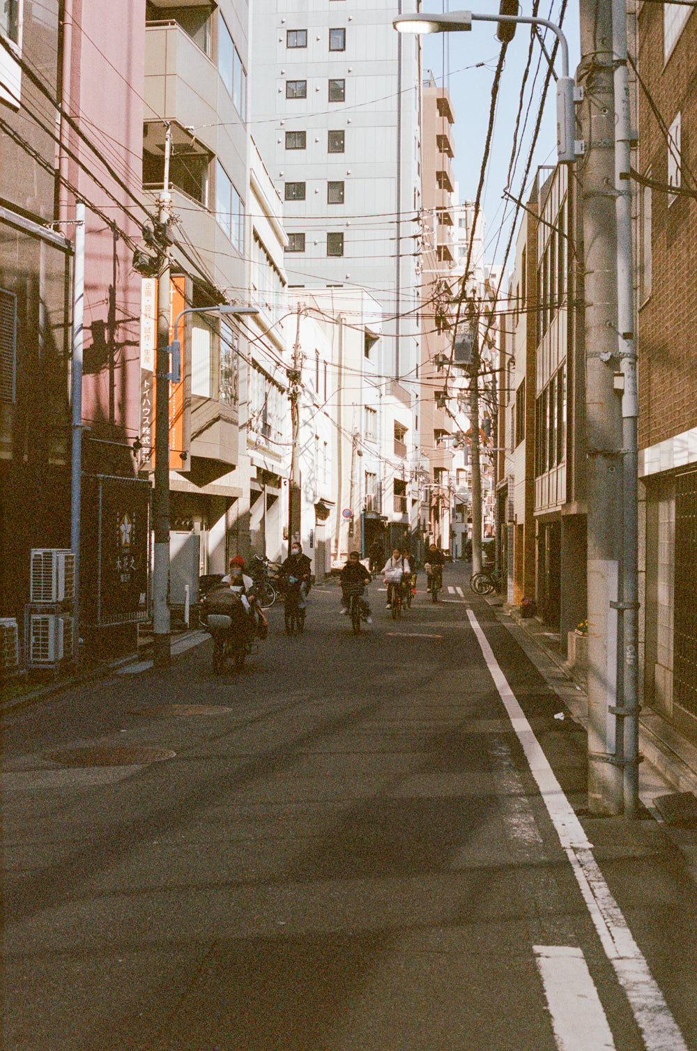 Narrow street in an urban area with tall buildings and people on motorcycles.