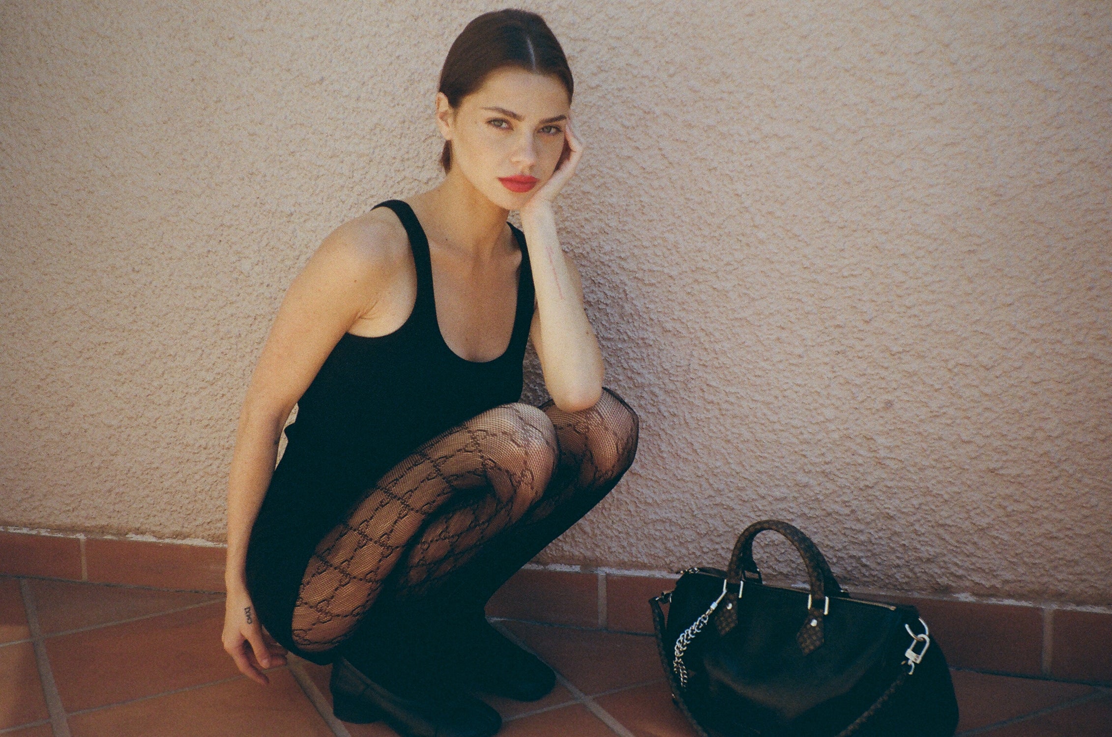 Woman crouching down wearing all black with a handbag