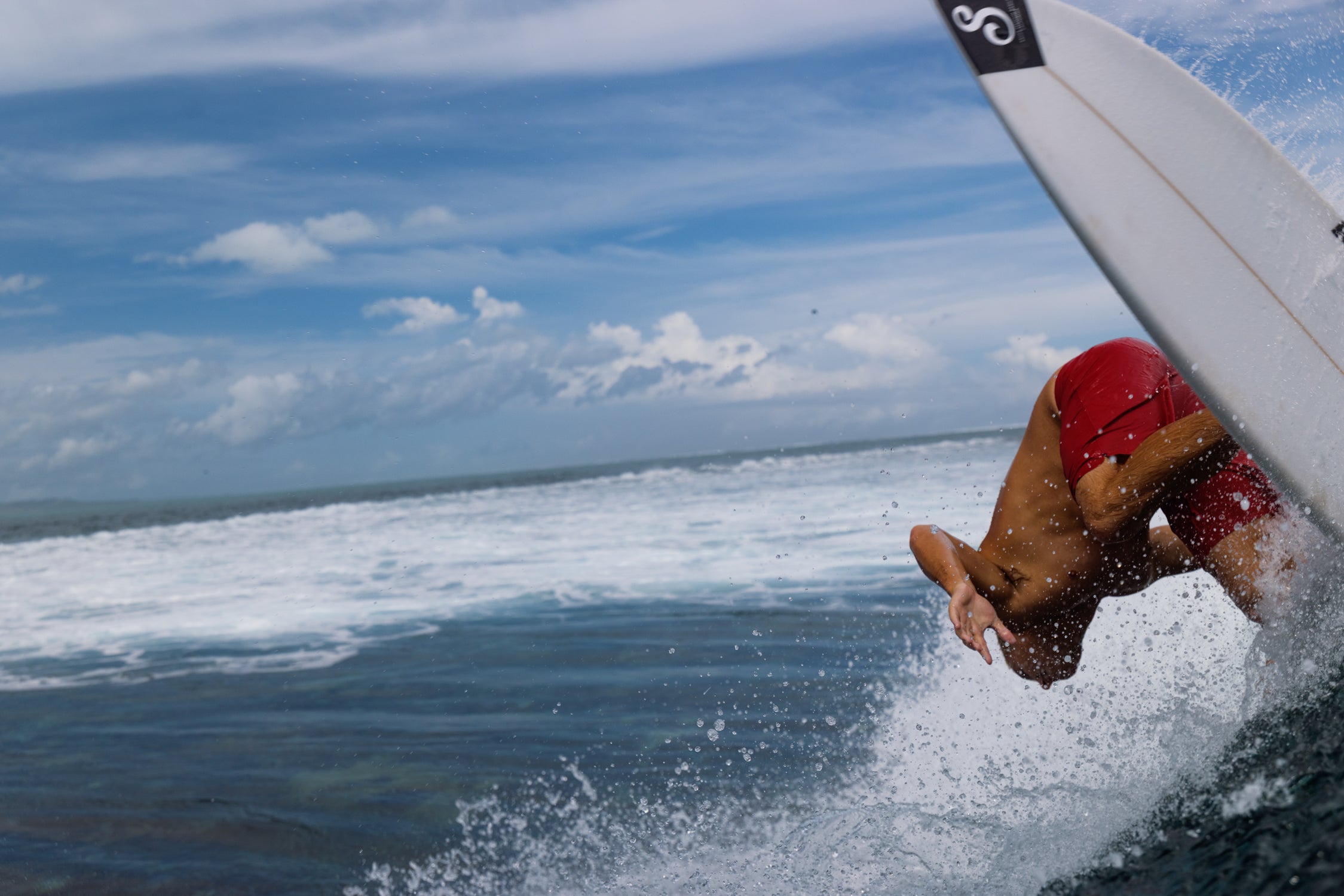 Person surfing with a red helmet on a wave, blue sky with clouds in the background