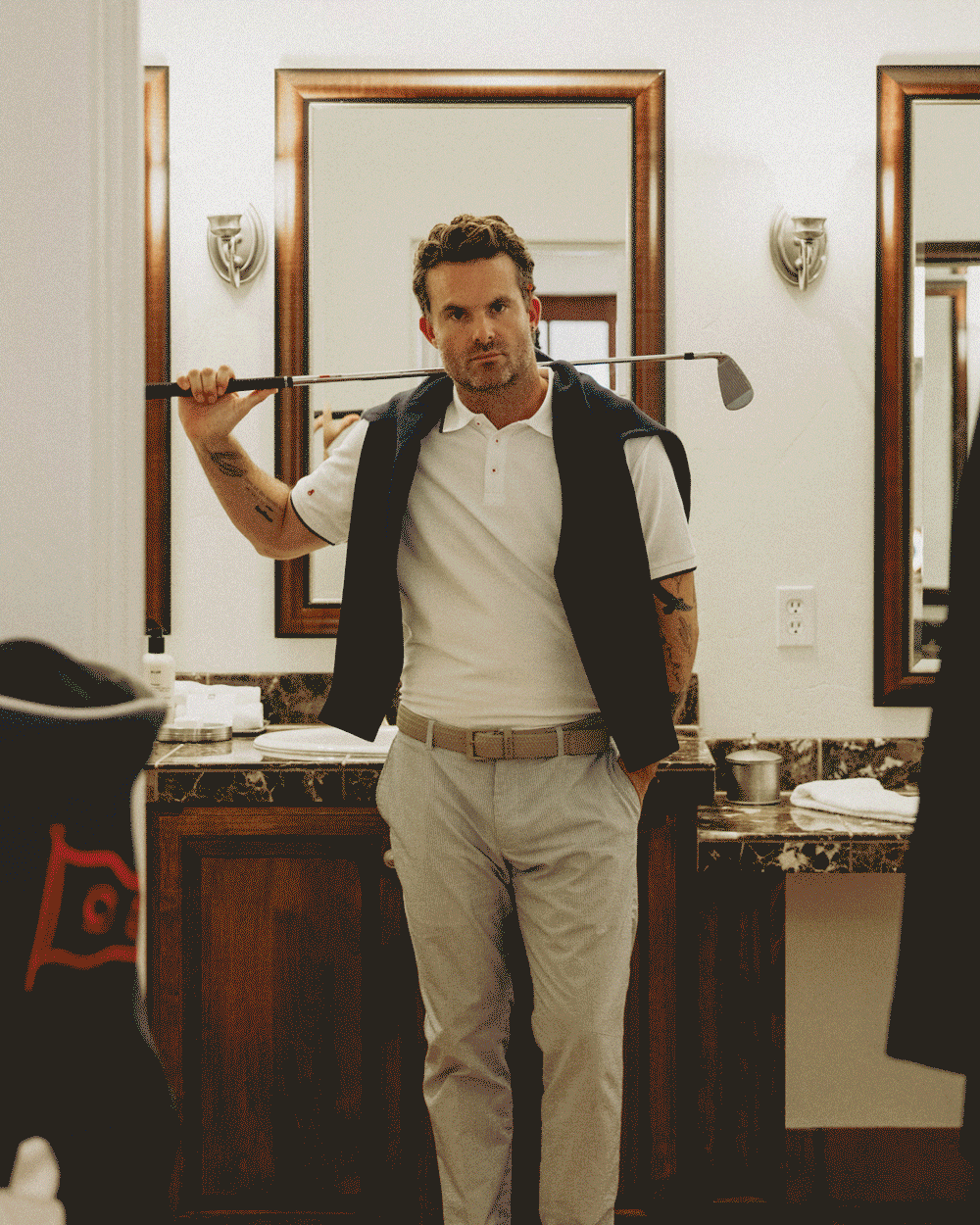 Alternating images of a man taking photos, playing golf, playing tennis, surfing, flying in a private jet, a model walking across a street with dogs. 
