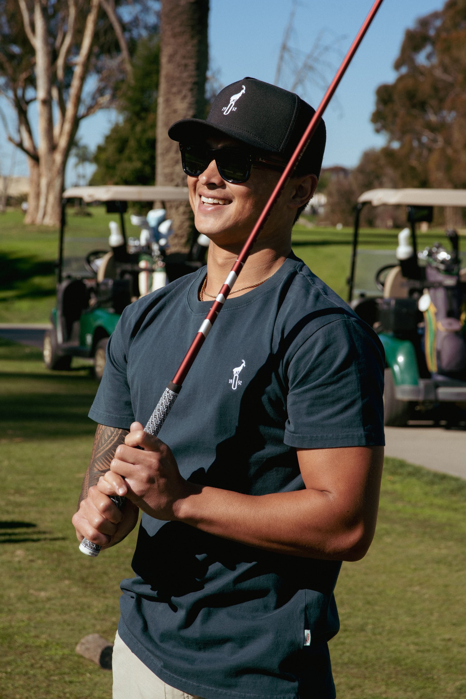 Person holding a golf club on a golf course with golf carts and trees in the background