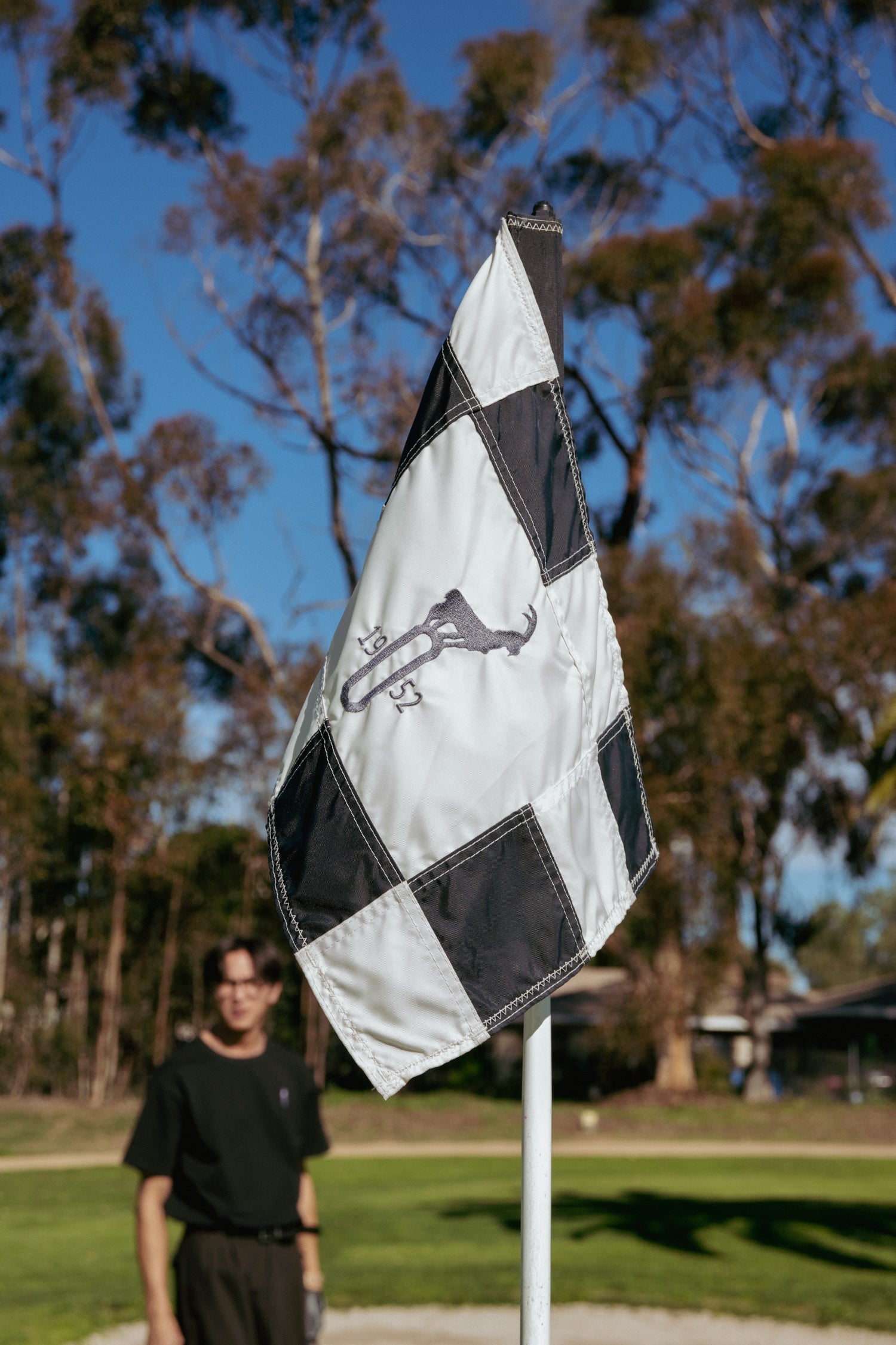 Person standing next to a checkered flag with a symbol on it in an outdoor setting.