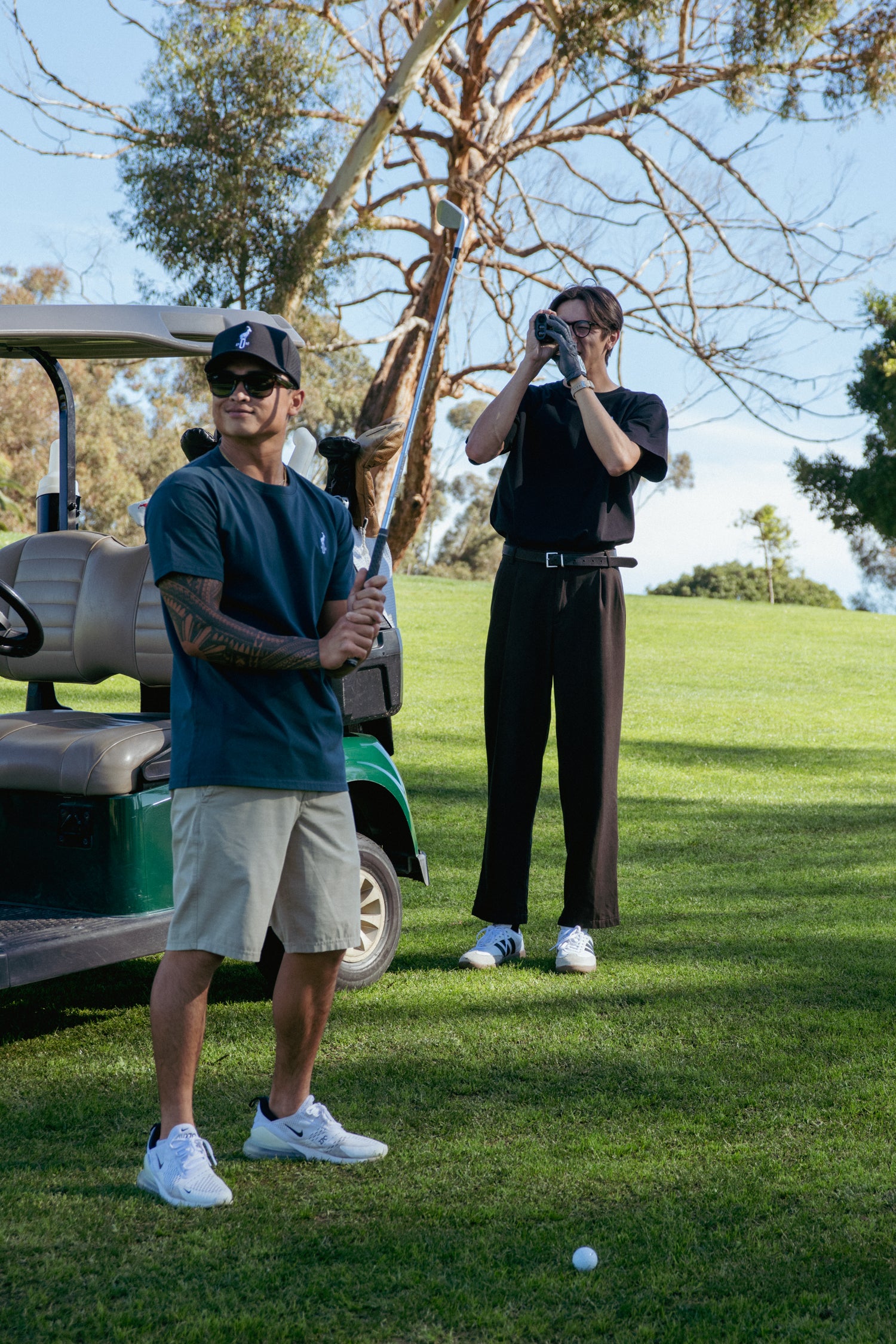 Two men on a golf course with one holding a golf club and the other taking a photo.