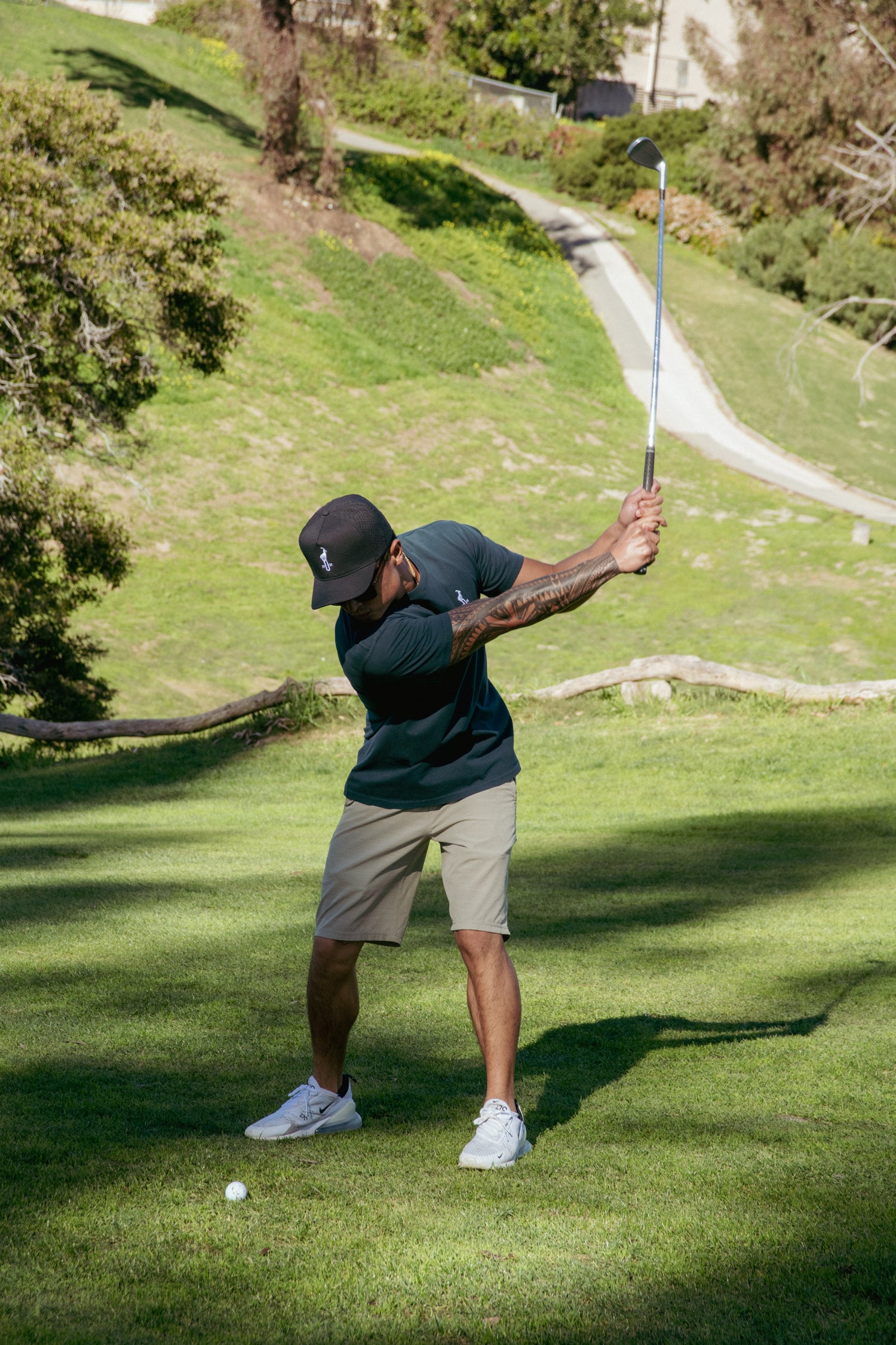 Man playing golf on a grassy course with trees and a path in the background