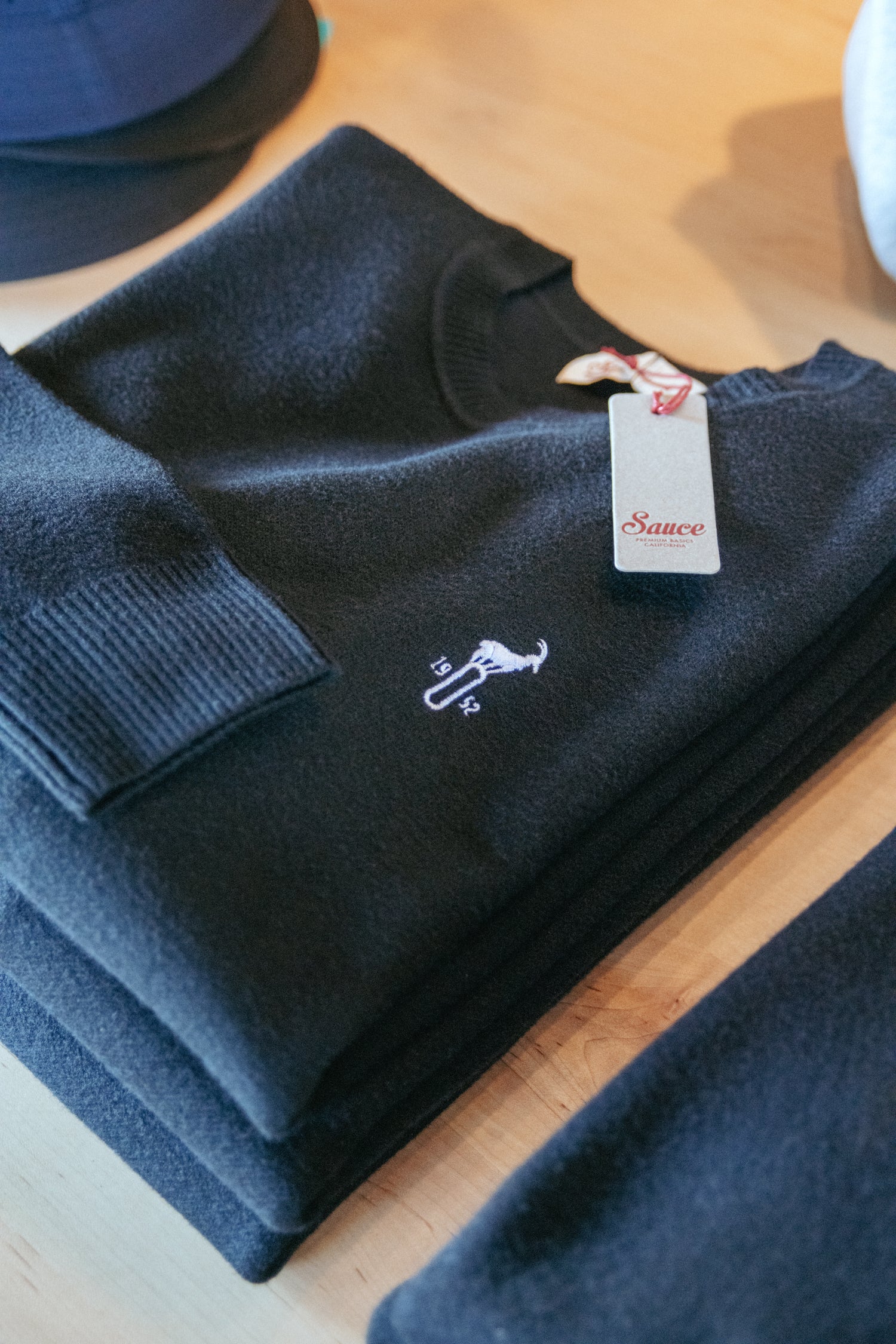 Folded navy blue sweater with a brand tag on a wooden surface