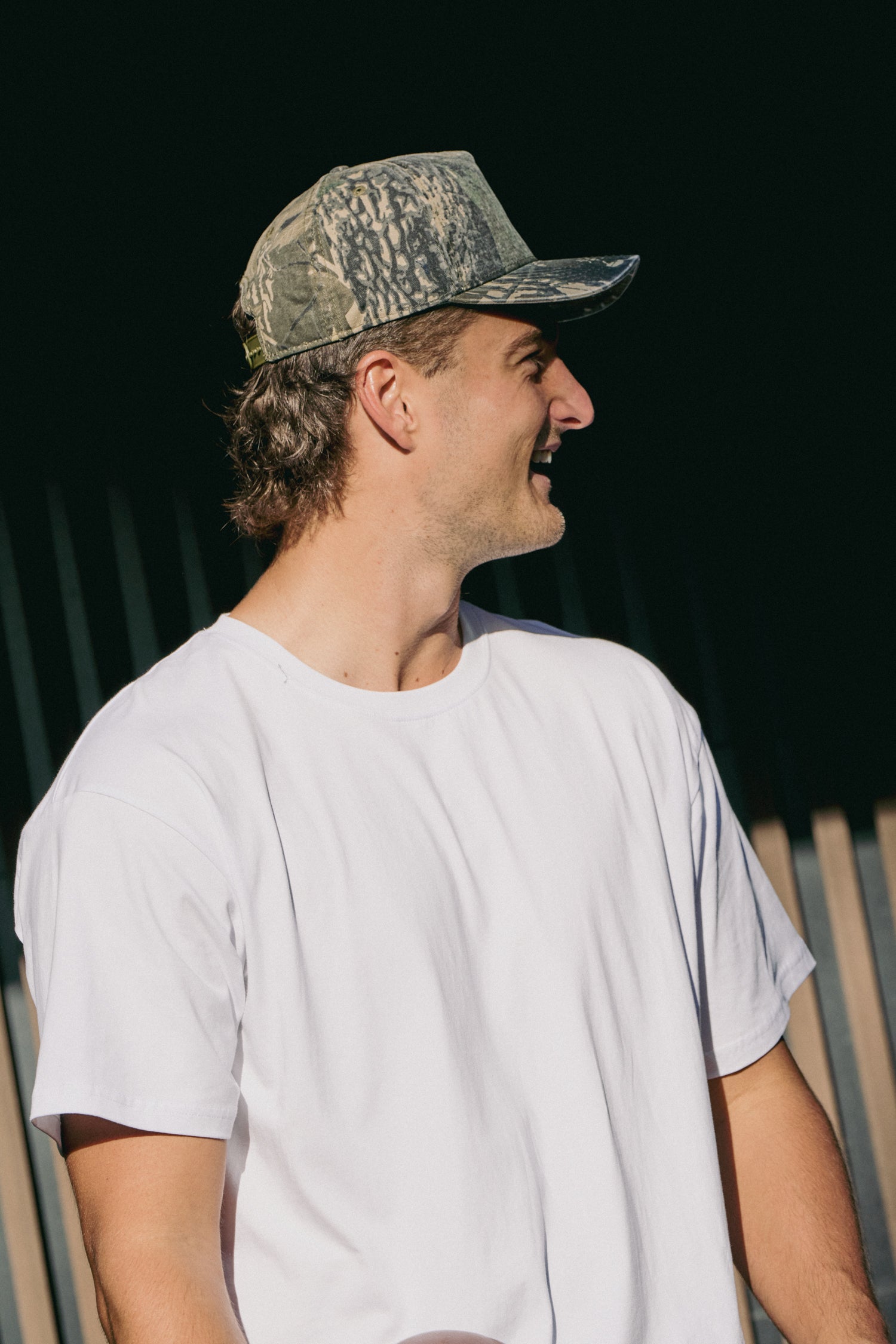 Man wearing a camouflage cap and white t-shirt against a dark background