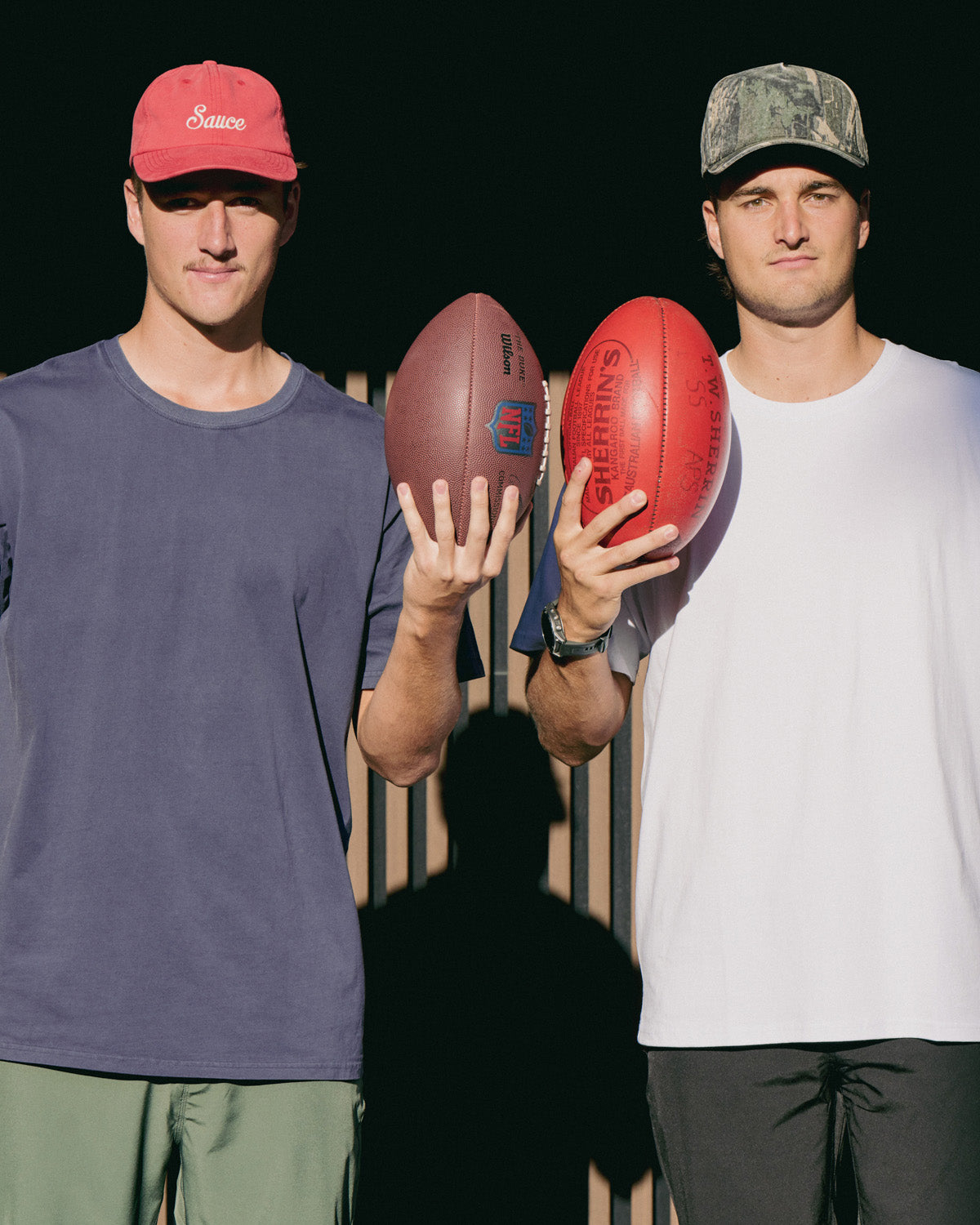 Two men holding footballs with a dark background
