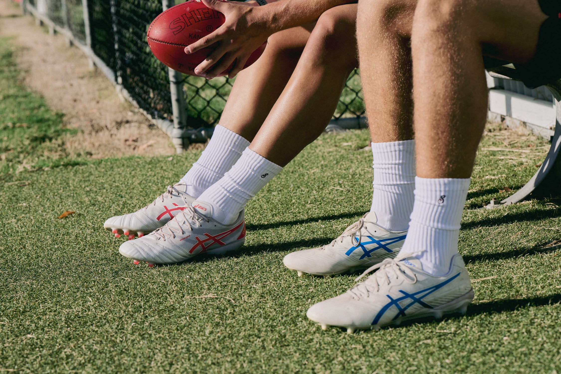 Two pairs of feet wearing white athletic shoes with colorful accents on a grassy field.