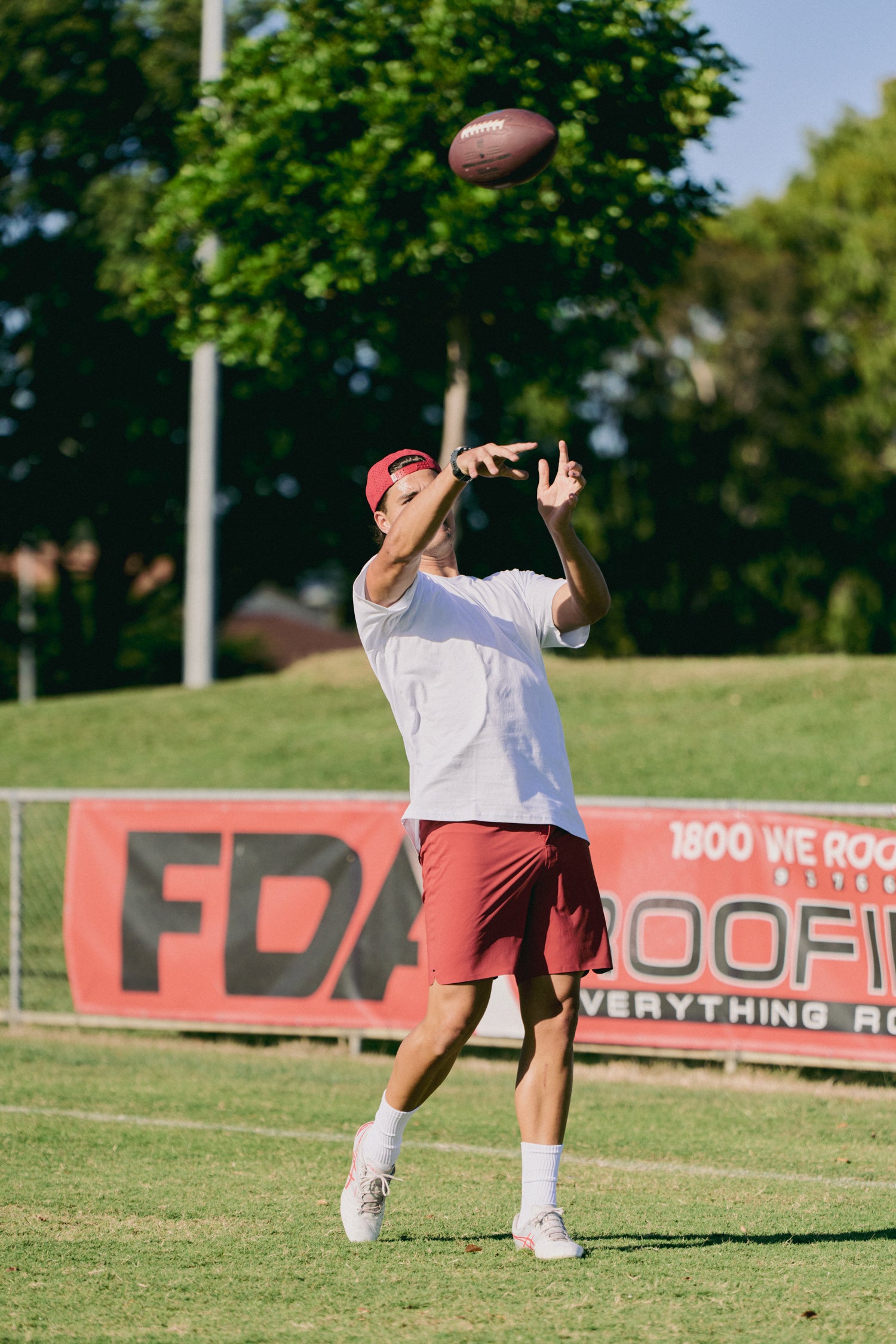 Person catching a football on a grassy field with trees in the background