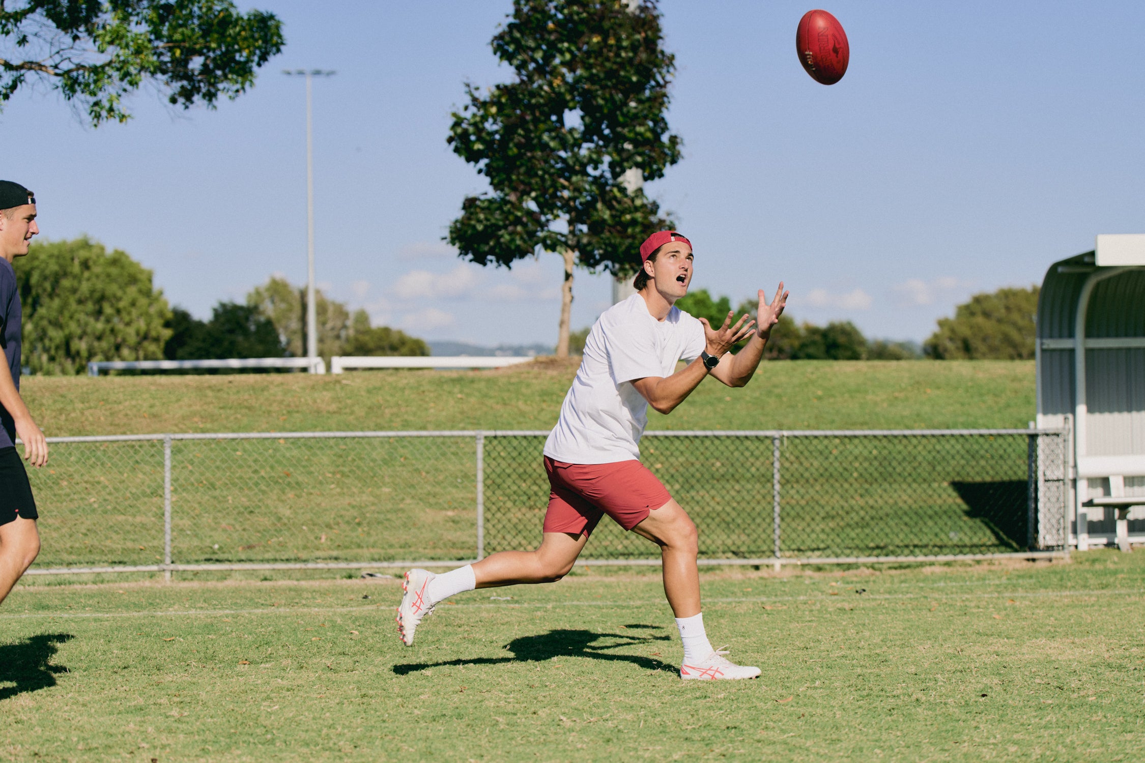Person playing football on a grassy field with trees and a fence in the background