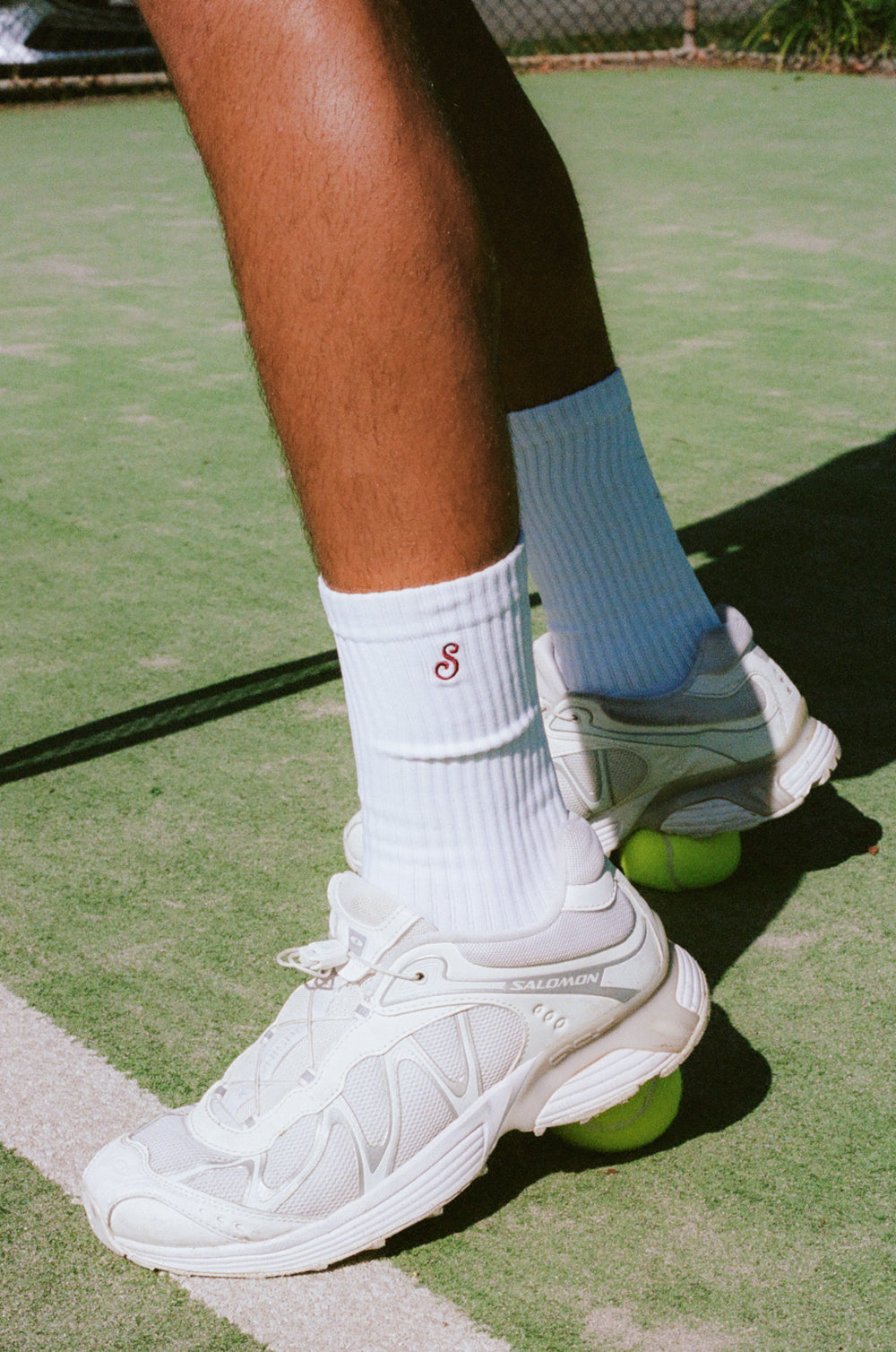 Tennis player's feet on a tennis court with white shoes and socks.