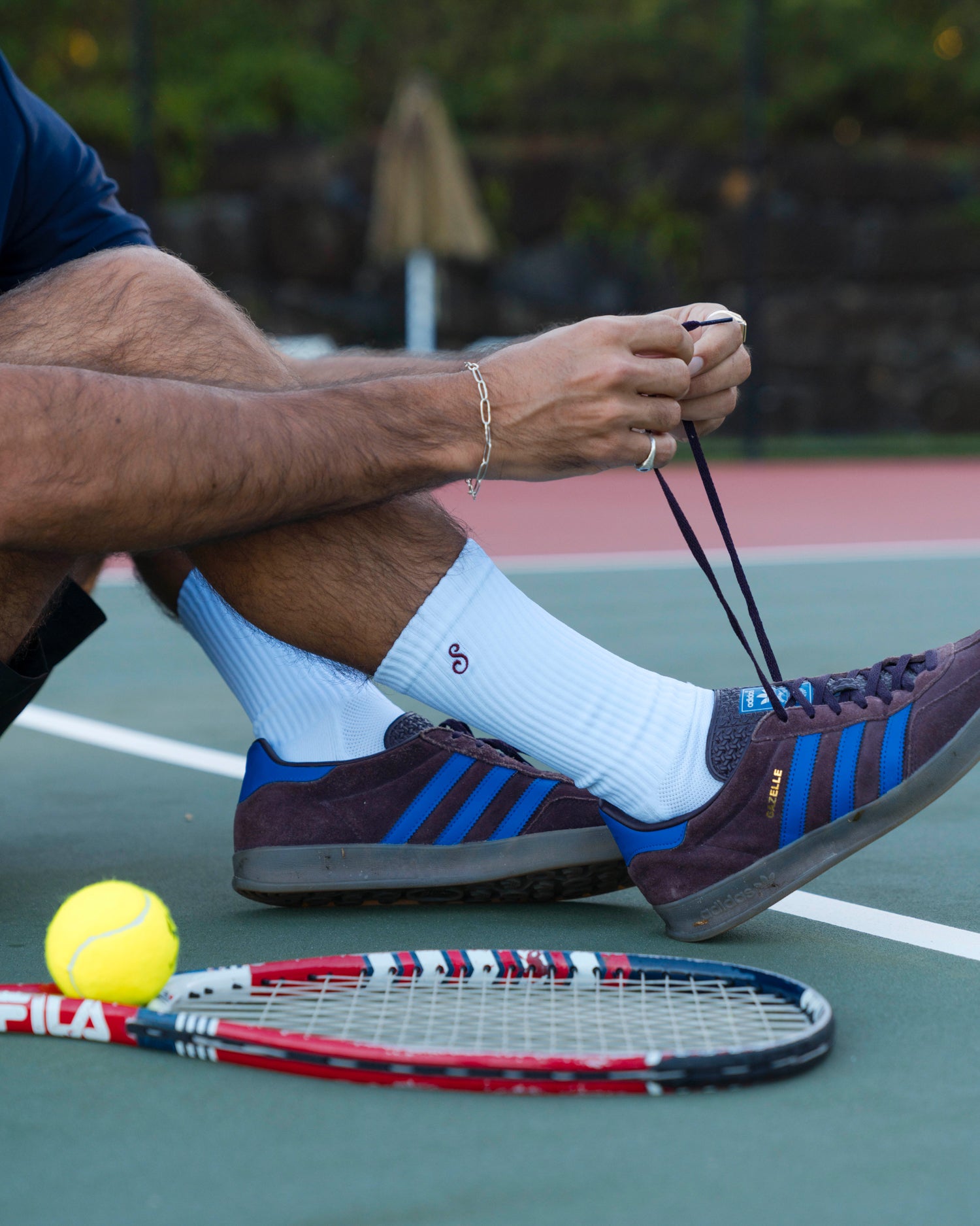 Person on a tennis court with a racket and ball, wearing Adidas shoes.