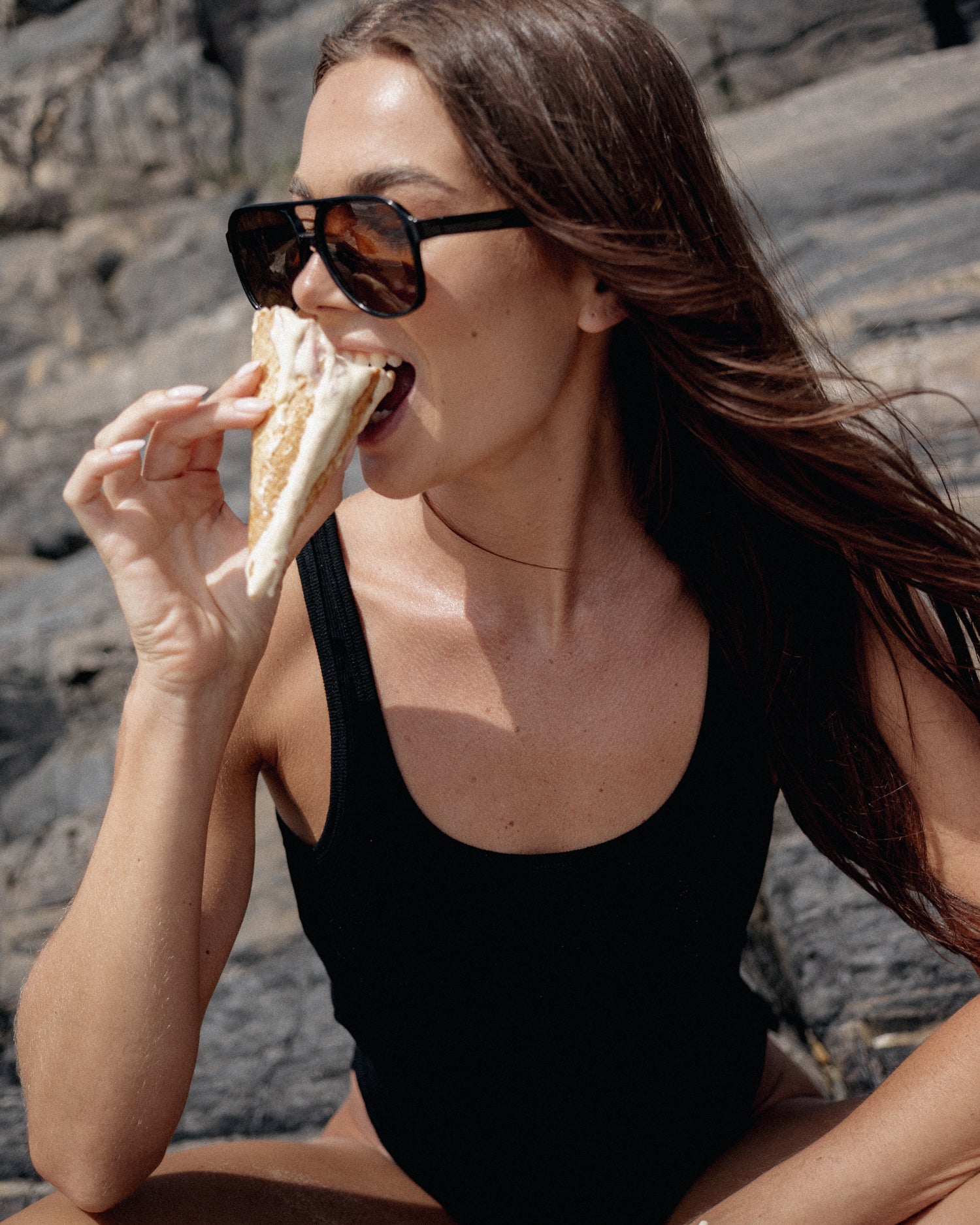 Woman in a black swimsuit eating aa ice cream outdoors.
