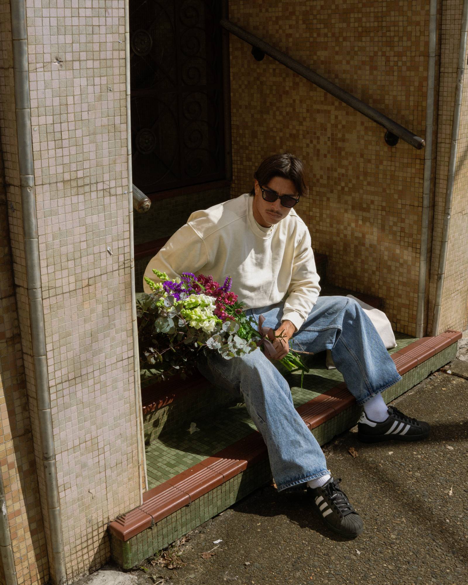 Person sitting on a bench with flowers, wearing sunglasses and casual clothing.