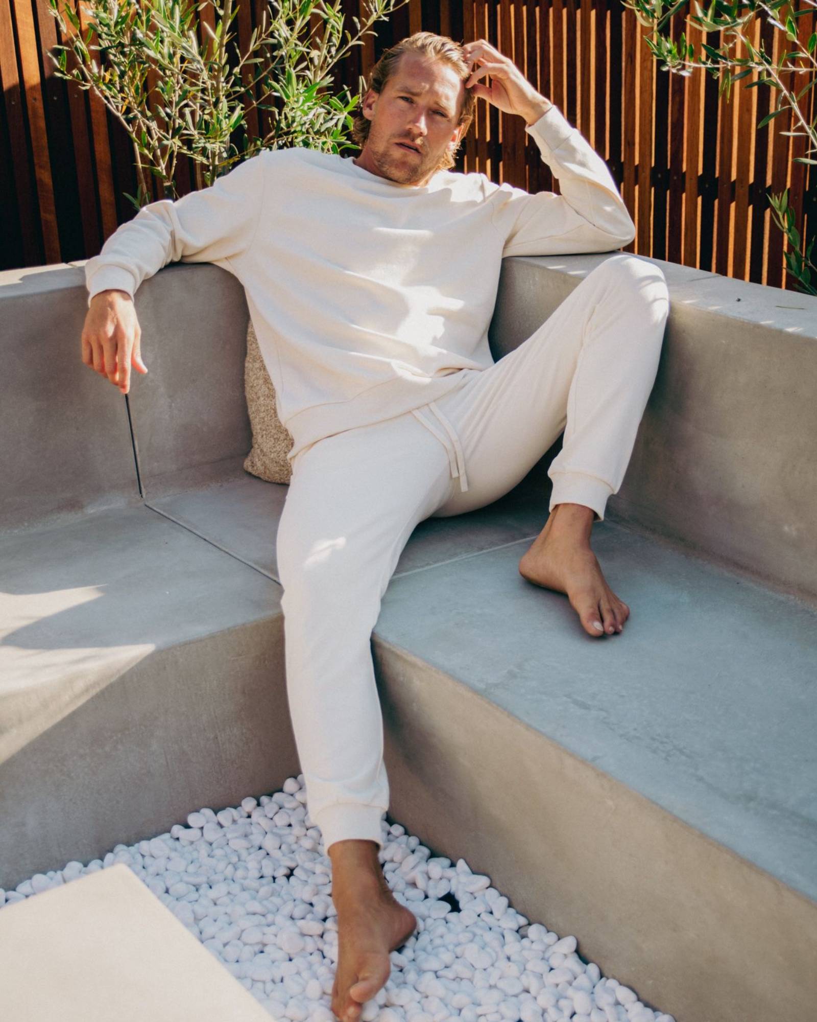Man in white loungewear sitting on a modern outdoor sofa with plants in the background
