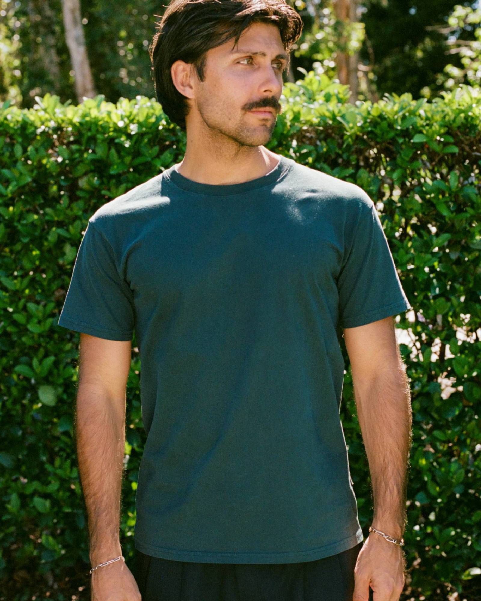 Man wearing a green t shirt standing in front of a garden wall