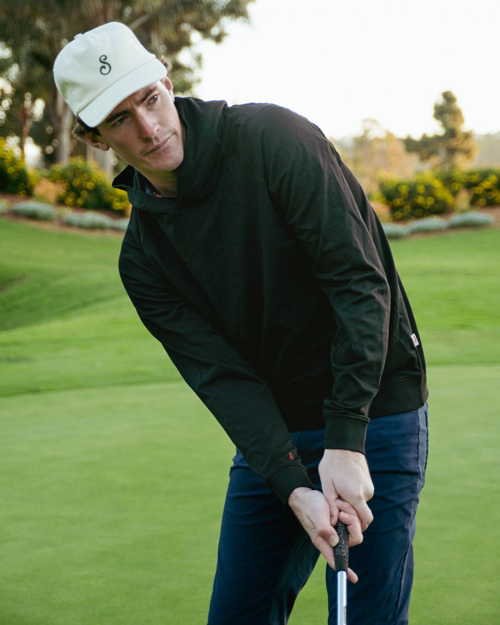 Man in black jacket and white cap playing golf on a green course