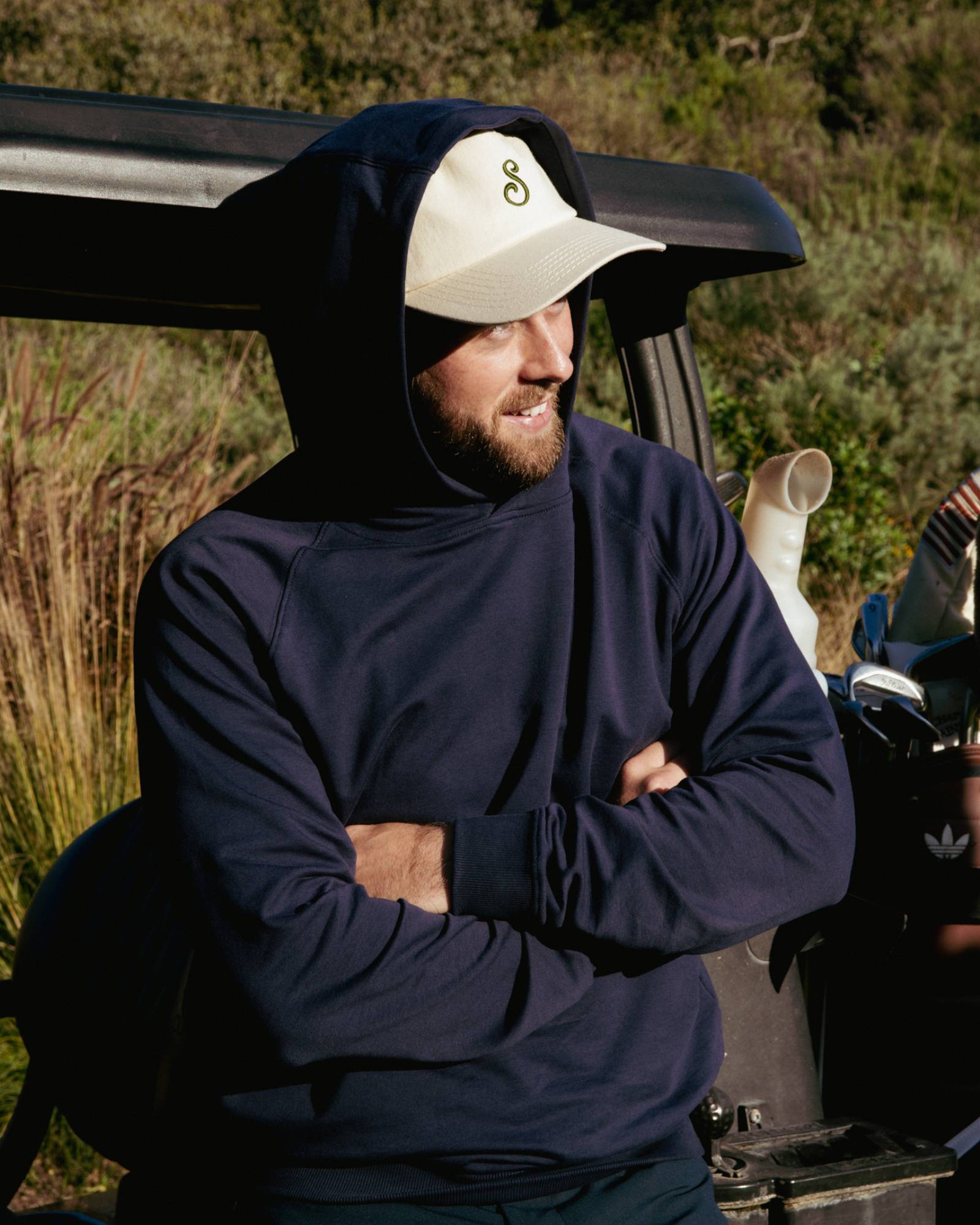 Man wearing a navy hoodie and cap leaning on a golf cart